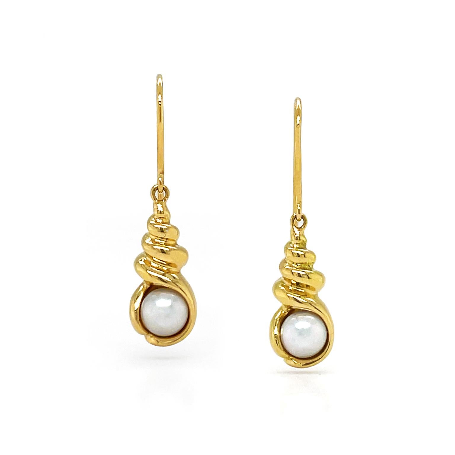 18k yellow gold creates an aquatic aura as it forms a seashell. Descending from the French-wire hooks is a spire-topped shell with an open round base with an Akoya pearl nesting inside. Craftsmanship includes ridges on the spire for depth and