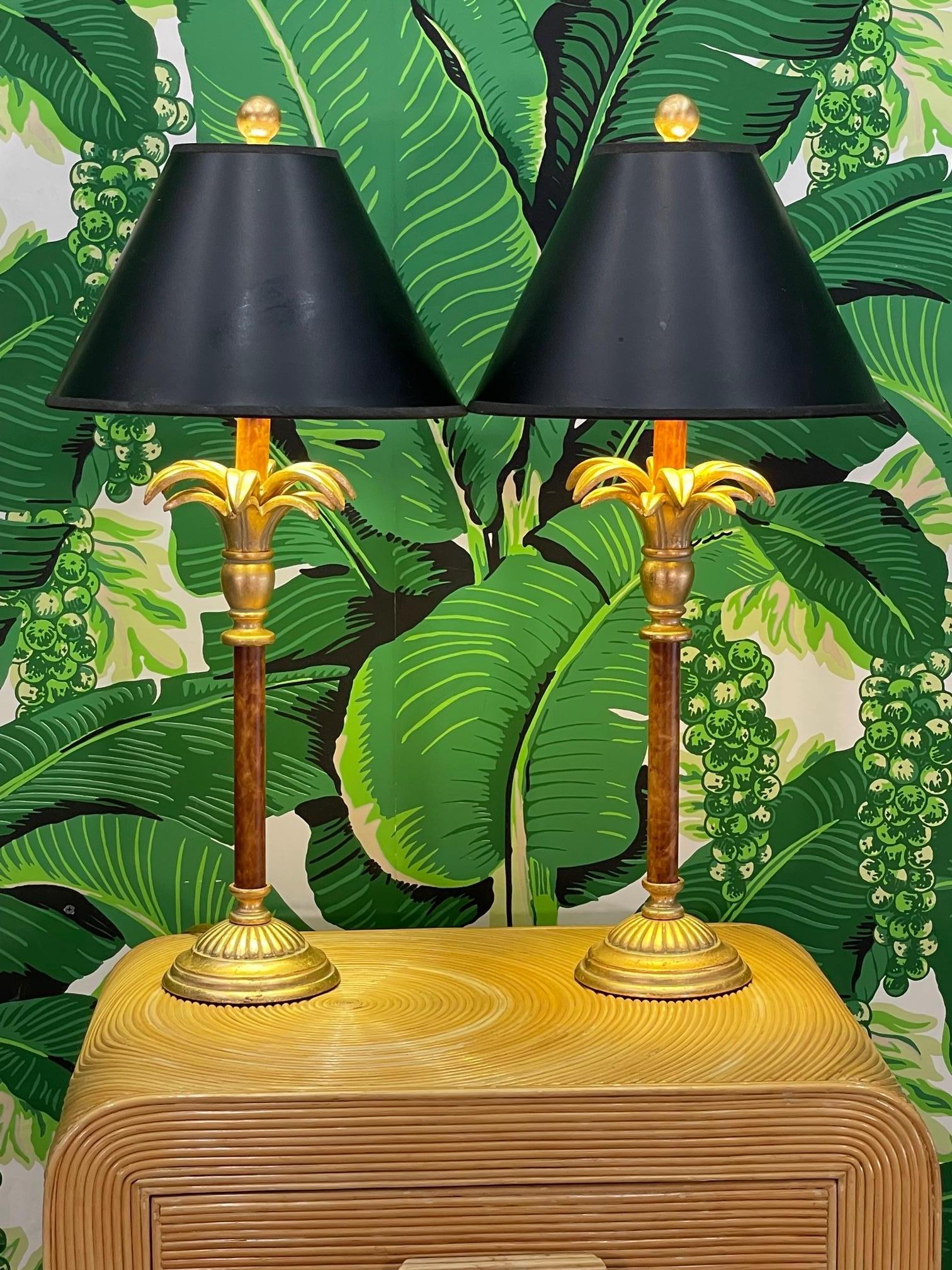 Pair of table lamps feature a palm tree motif with a bright gold finish and black shades. Good vintage condition with imperfections consistent with age, see photos for condition details. 
 