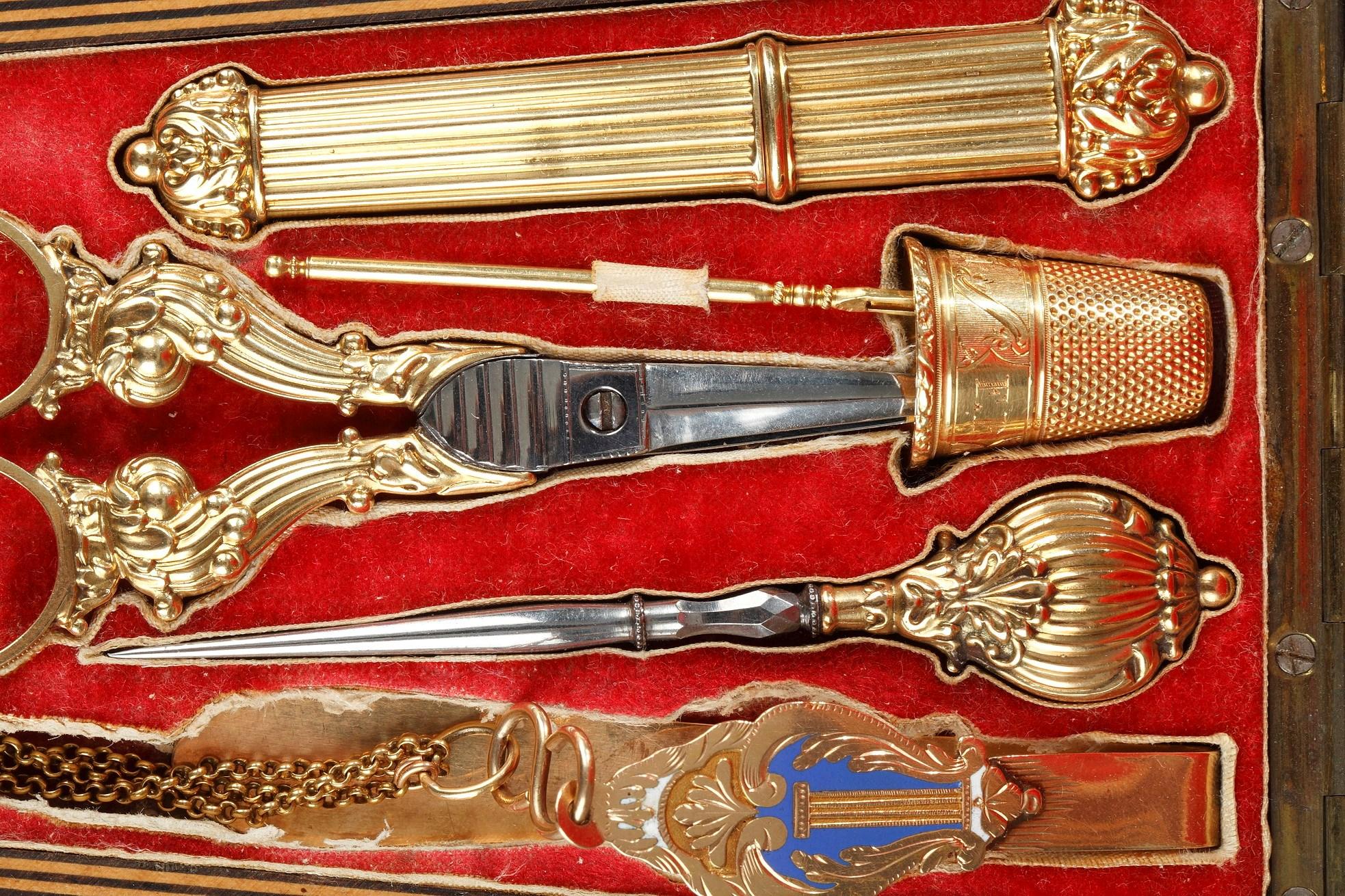A Restauration set presented in a monogrammed trapezoidal case made of light wood. The vanity case includes a gold needle case decorated with flutes, a dice and a wool needle, a gold and steel punch and a pair of gold and steel scissors.

In the