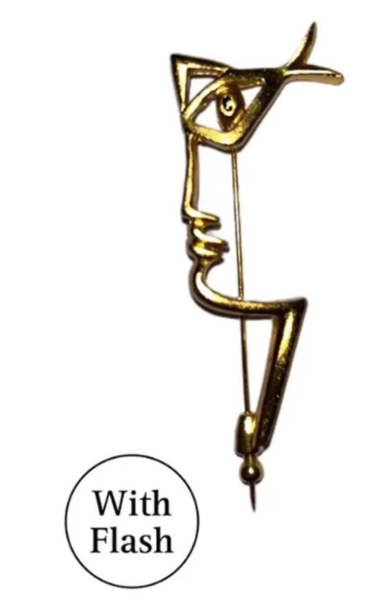 This gold-toned brooch is inspired by the work of the French poet Jean Cocteau, known for simple but expressive drawings. This minimalist and modern brooch is the profile of fishermen. The eye of each fisherman is black at its centre, and the shape