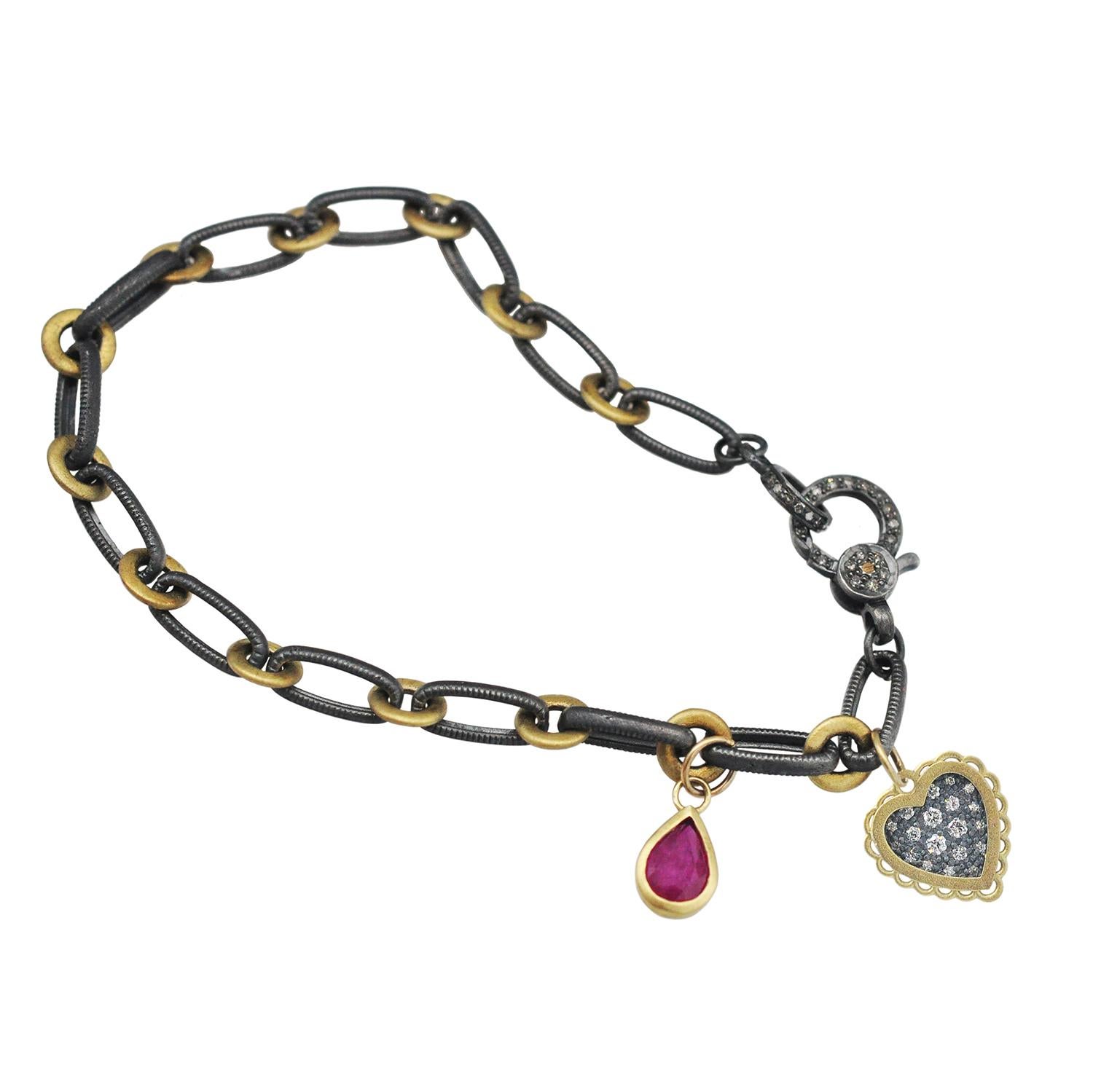 Pave set diamonds, mixed metals, and a juicy pink ruby make this charm bracelet a real show-stopper!
Oxidized sterling silver and 18k yellow gold links are connected with a pave set diamond clasp and adorned with two beautiful charms: a 1/2
