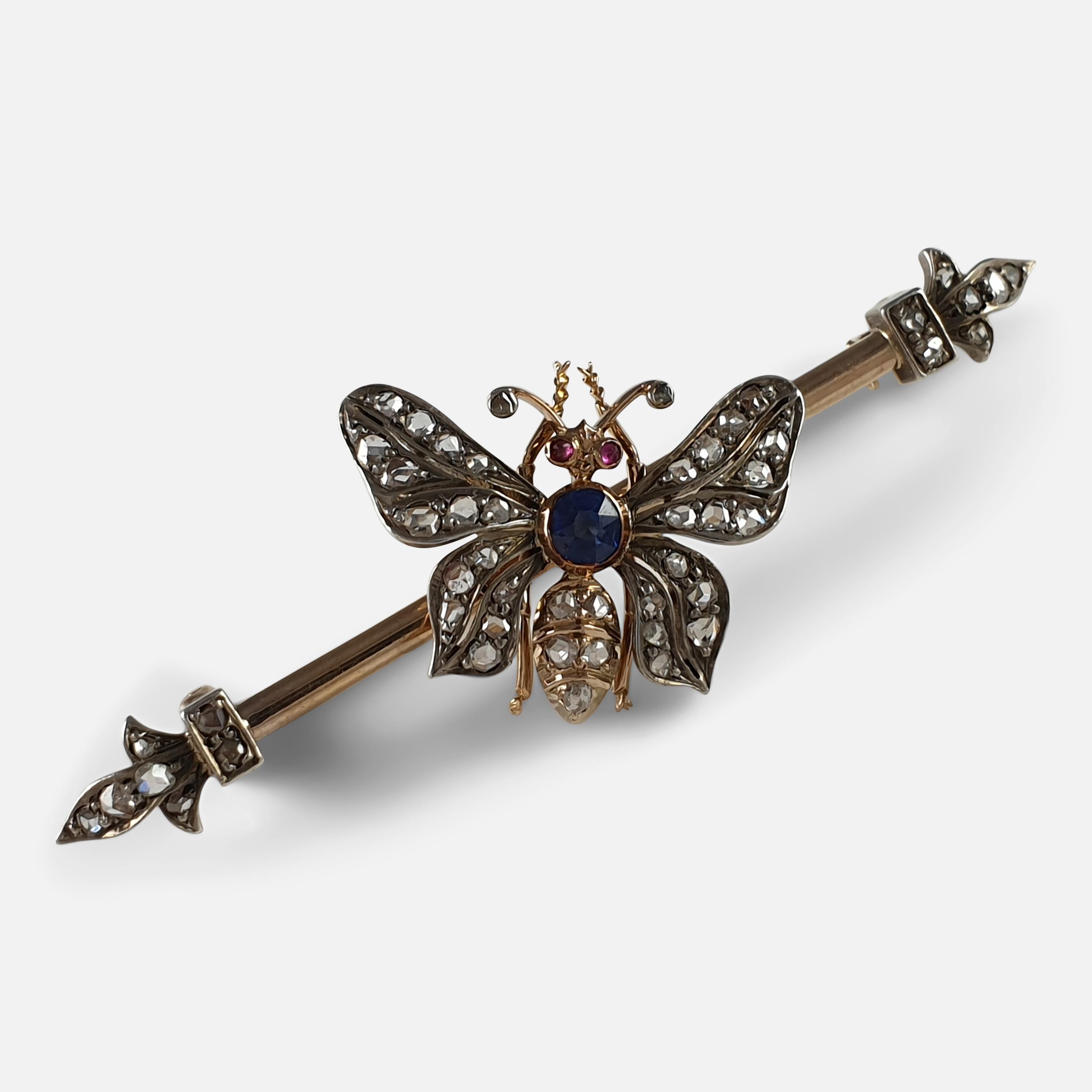 A 19th century 18k yellow gold, silver fronted, ruby, sapphire, and diamond butterfly brooch, circa 1895. The brooch is designed as a rose-cut diamond butterfly with circular-cut ruby eyes, cushion-shaped sapphire thorax, to a polished bar with