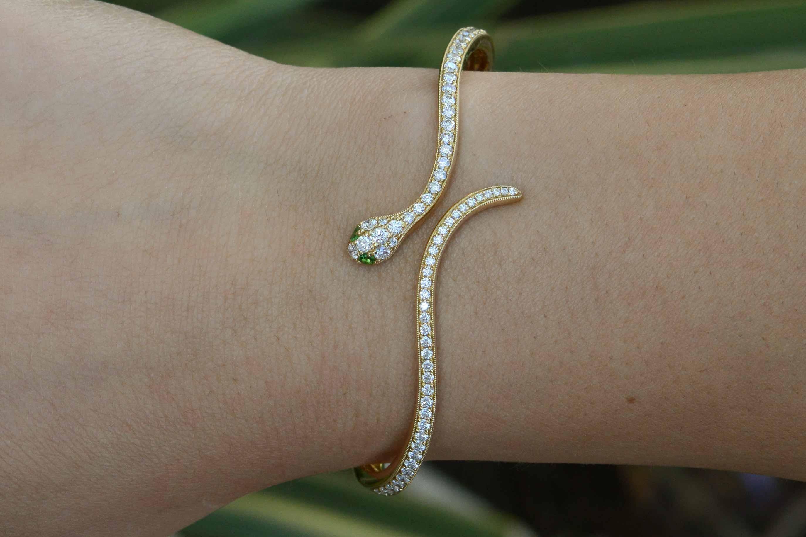 An alluring yellow gold snake bangle bracelet encrusted with shimmering diamond pavé of nearly 1.50 carats. The hinged cuff, reminiscent of Cleopatra, features twinkling green Tsavorite garnet eyes. Created in an Egyptian revival style with great