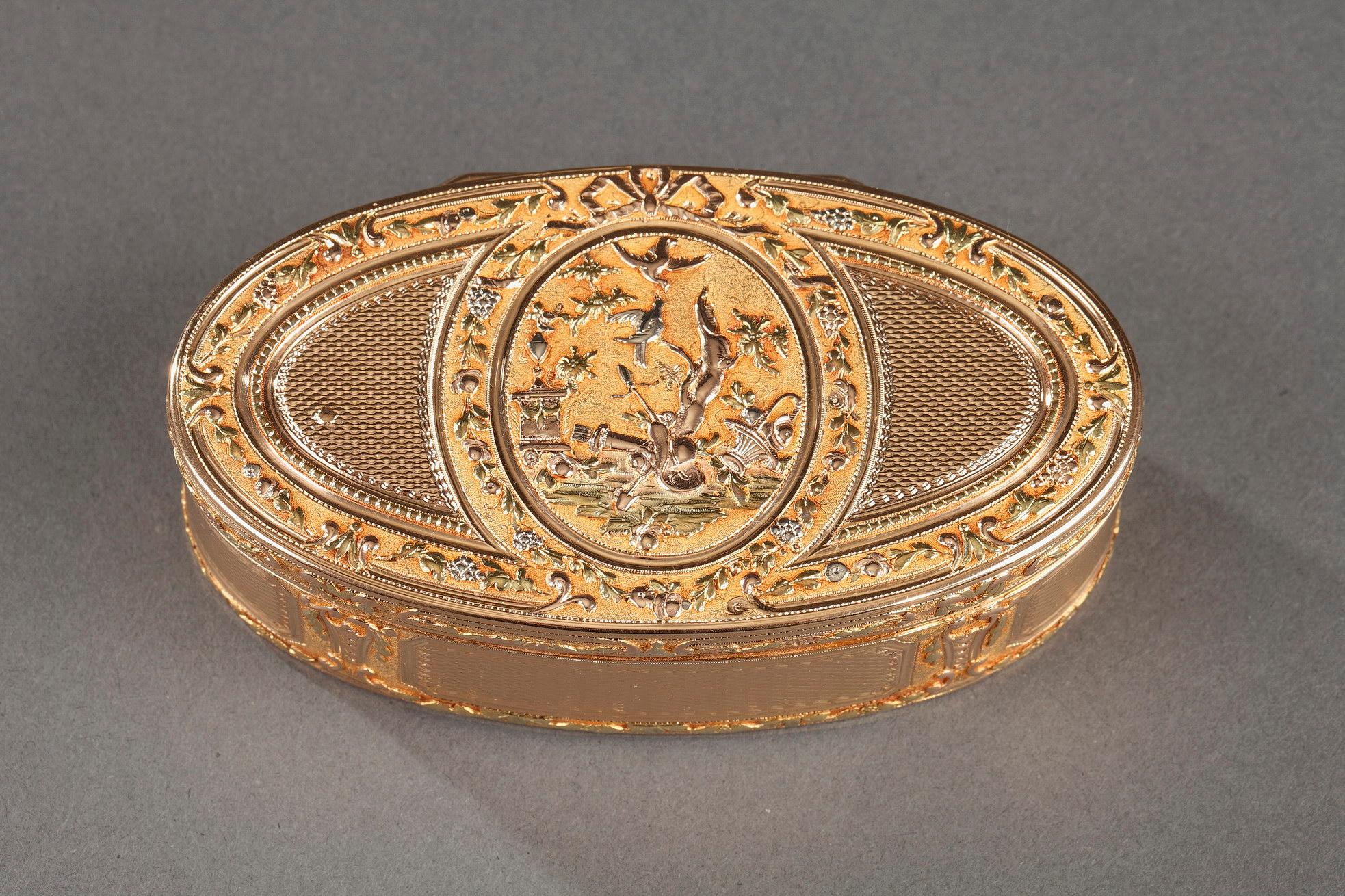 Oval snuff box featuring in gold of several tones.. The hinged lid is decorated with a central medallion featuring two doves near an altar on a landscape background. The doves that stand out against a background of amati gold. The doves, a symbol of