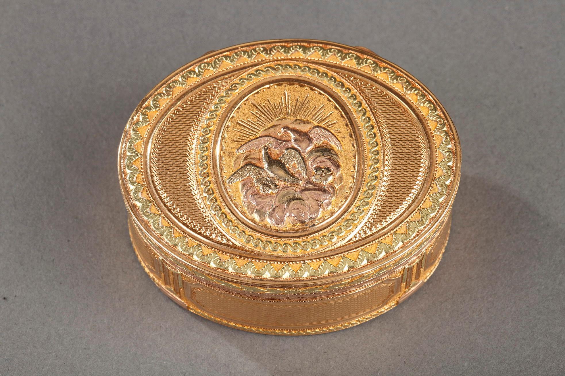 Oval snuff box featuring green, yellow, and pink gold. The hinged lid is decorated with a central medallion featuring two doves in a cloud with a rising sun behind them. The doves, a symbol of love and of Venus in particular, are set on a matte gold