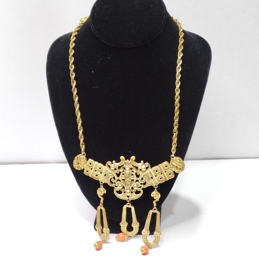 Get your hands on this stunning 1980s gold statement necklace! A large victorian style motif is the focal point of the necklace and features intricate engravings as well as three drops with gold pendants cascading from them. Orange stone charms