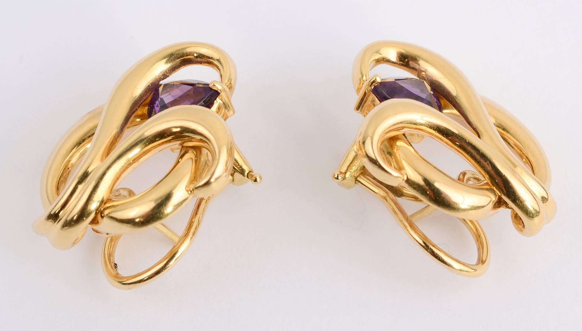 Very graceful 18 karat gold earrings in a swirl pattern highlighted with a faceted amethyst in a triangular shape. The backs are both clips and posts. 
The earrings are 1 inch long and 7/8 inches wide.