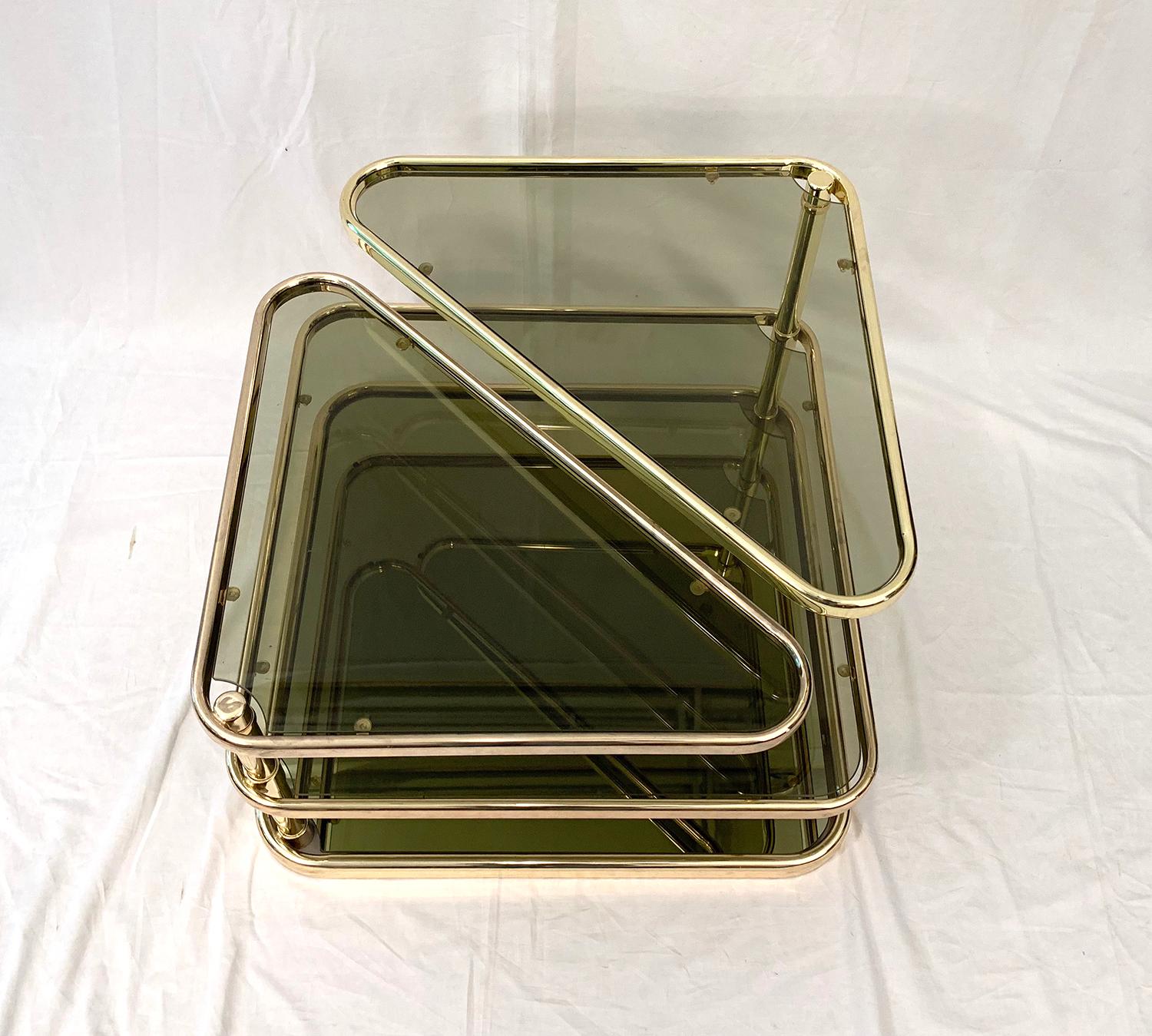 Very beautiful coffee table, composed of four trays whose two superiors are pivoting. The ground level plateau is in a golden mirror with a very slight green reflection and the three upper trays are in smoked glass. The metal structure is clad in