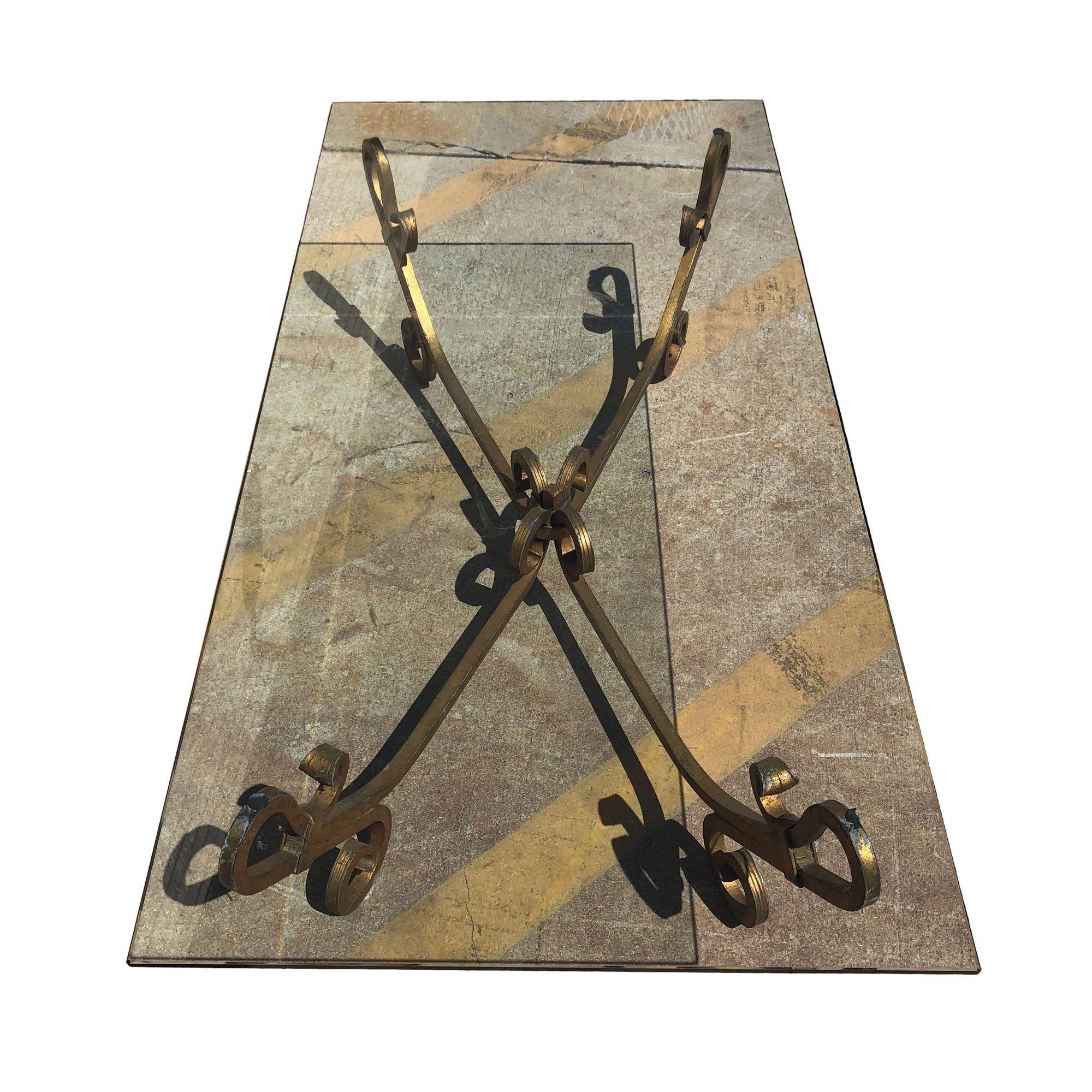 Table à cocktail en fer forgé doré, avec un plateau en verre, datant du milieu du siècle dernier. La base en fer forgé est formée de motifs en volutes qui s'étendent de haut en bas avec une finition luxueuse de tonalité dorée qui rehausse son