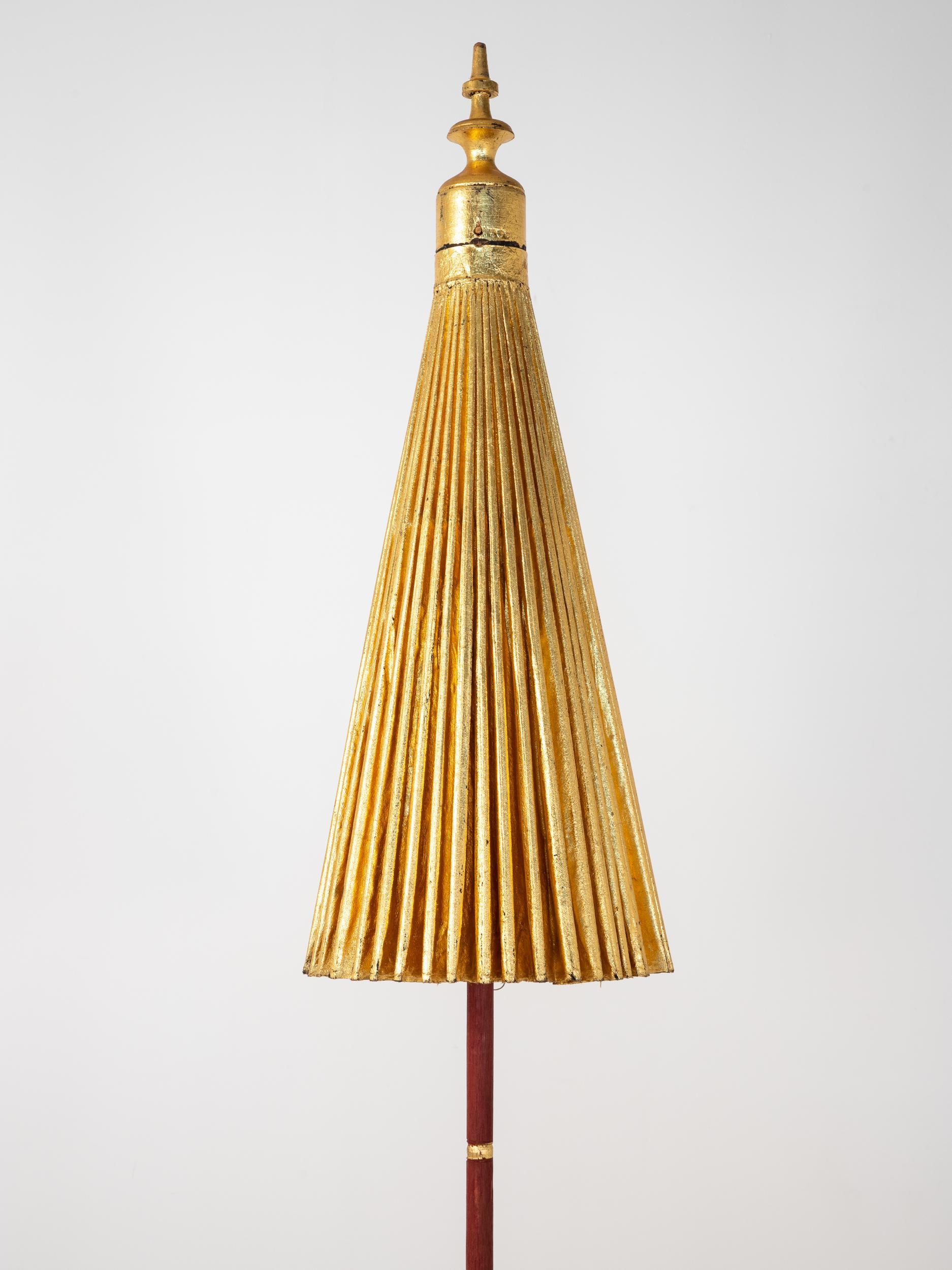 Stunning sun umbrella with a gilt exterior and a painted wood column with a gold finial at the top. The gold umbrella opens to reveal a brilliant pattern of color created by woven threads anchored by a black interior. The column of the umbrella is