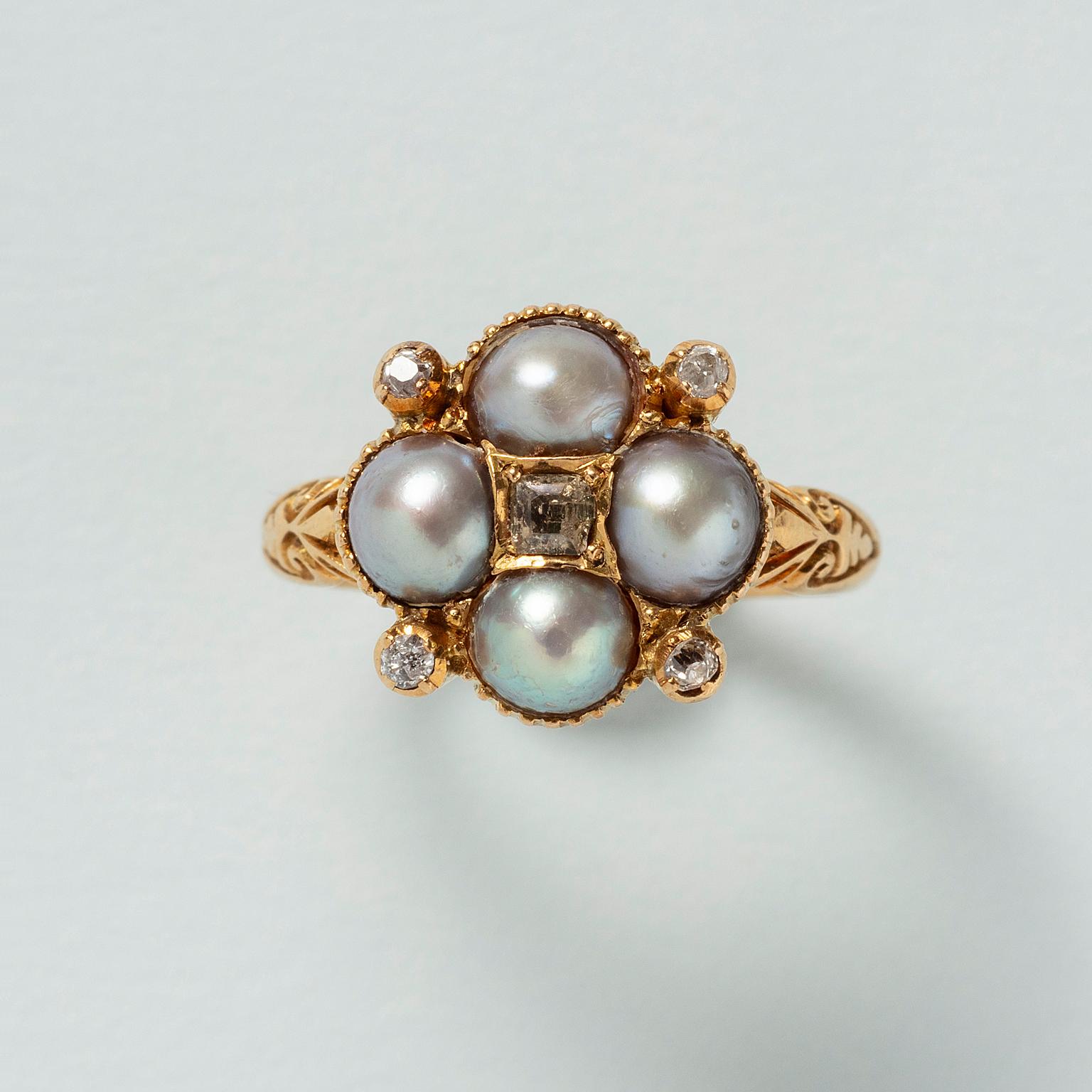 An 18 carat yellow gold ring set with four half round, grey pearls set in a clover shape with five old cut diamonds in between and at the heart, decorated with floral engravings and curls on the sides of the shank. England, circa 1890.

weight: 6.11