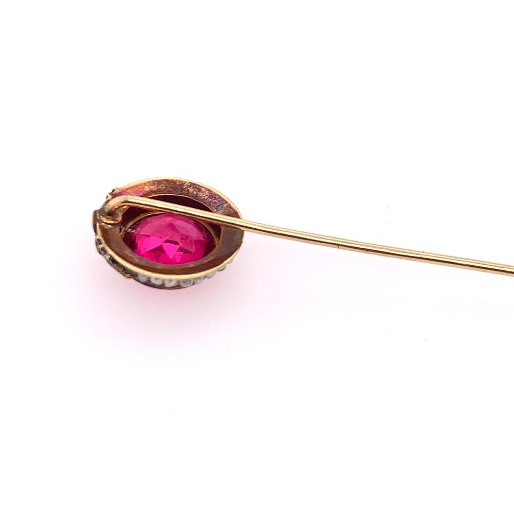 A gold pink imitation sapphire pin set with white seed pearls and a floral design.