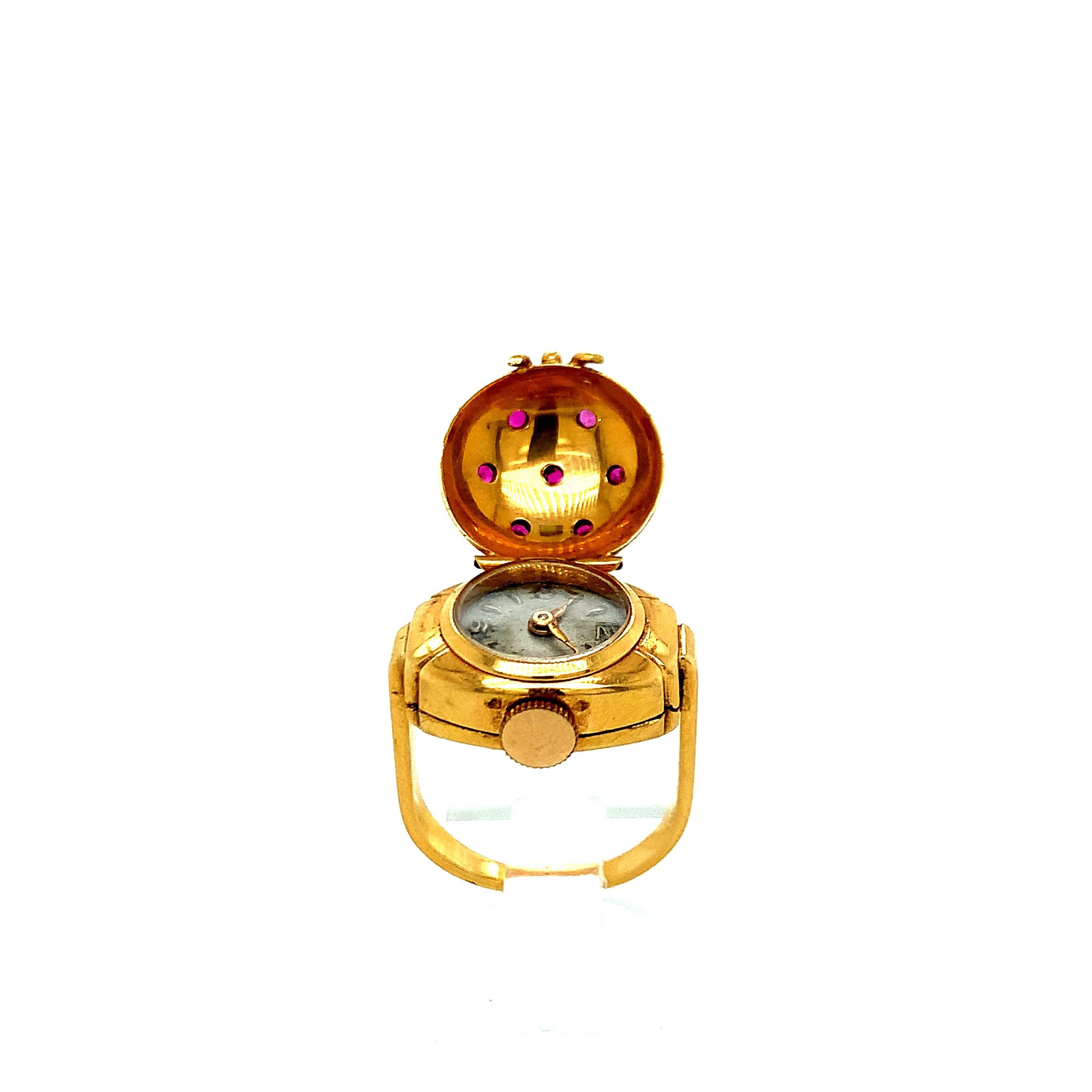 An 18 karat yellow gold covered watch ring with seven round rubies. A watch appears when the top of the ring is opened. Stamped 59829. Total weight 10.1 grams. Size 4.25.