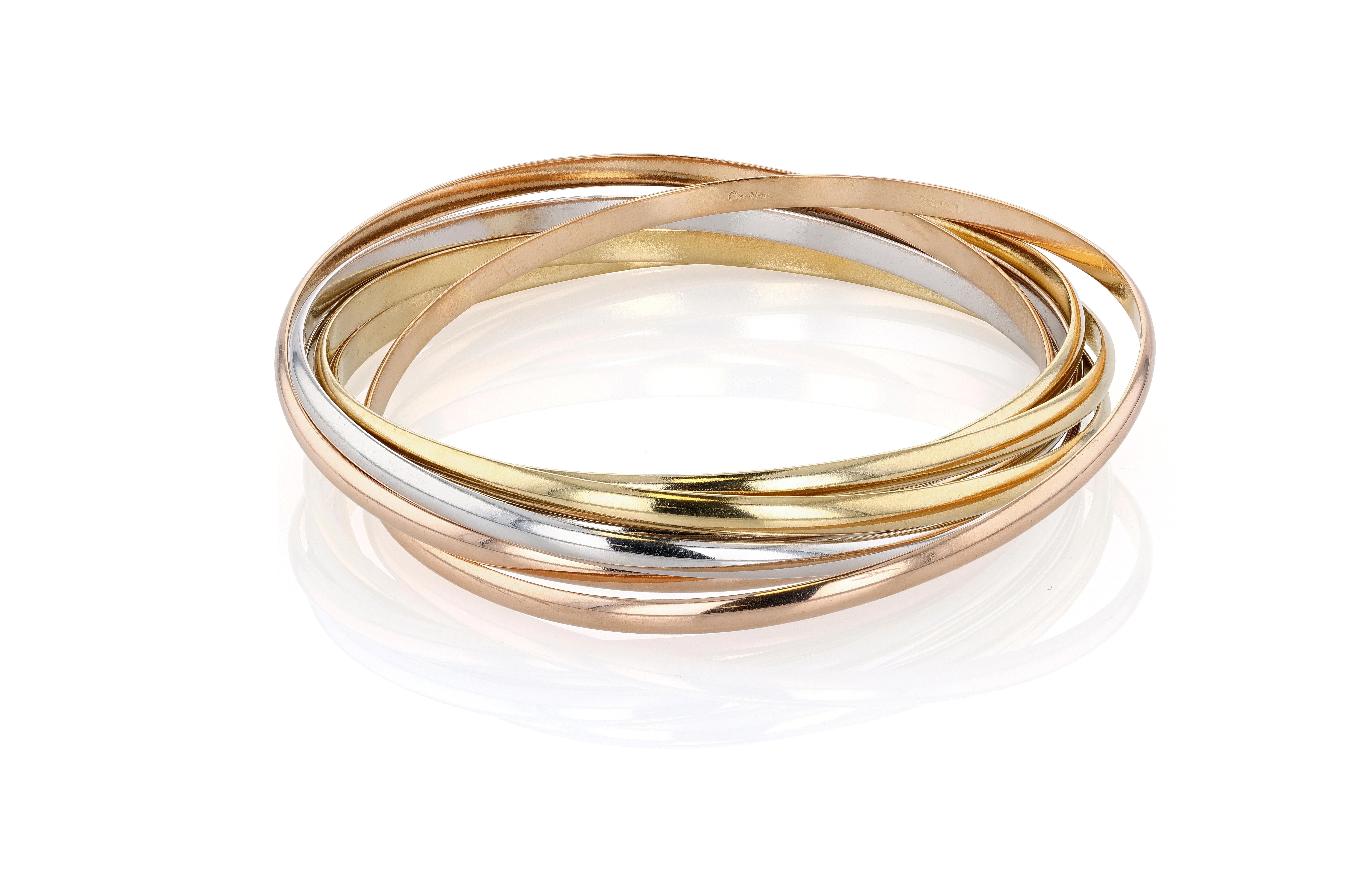Bangle Trinity di Cartier in oro giallo, bianco e rosa a sette file, referenza Cartier 13477J. Il Cartier Trinity fu creato nel 1924, presumibilmente per volere di Jean Cocteau che, ossessionato dagli anelli di Saturno, commissionò all'amico Jean