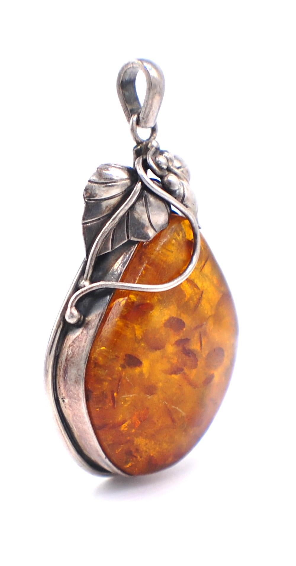 Flicks of Colored Amber incased in a bezel setting with leaf designed accent to artistically decorate this pendant.
The pendant measures 2-1/3 inch length with another 1/2 inch long chain bail. The width of pendant is 1-1/2 inches.
Colored amber are