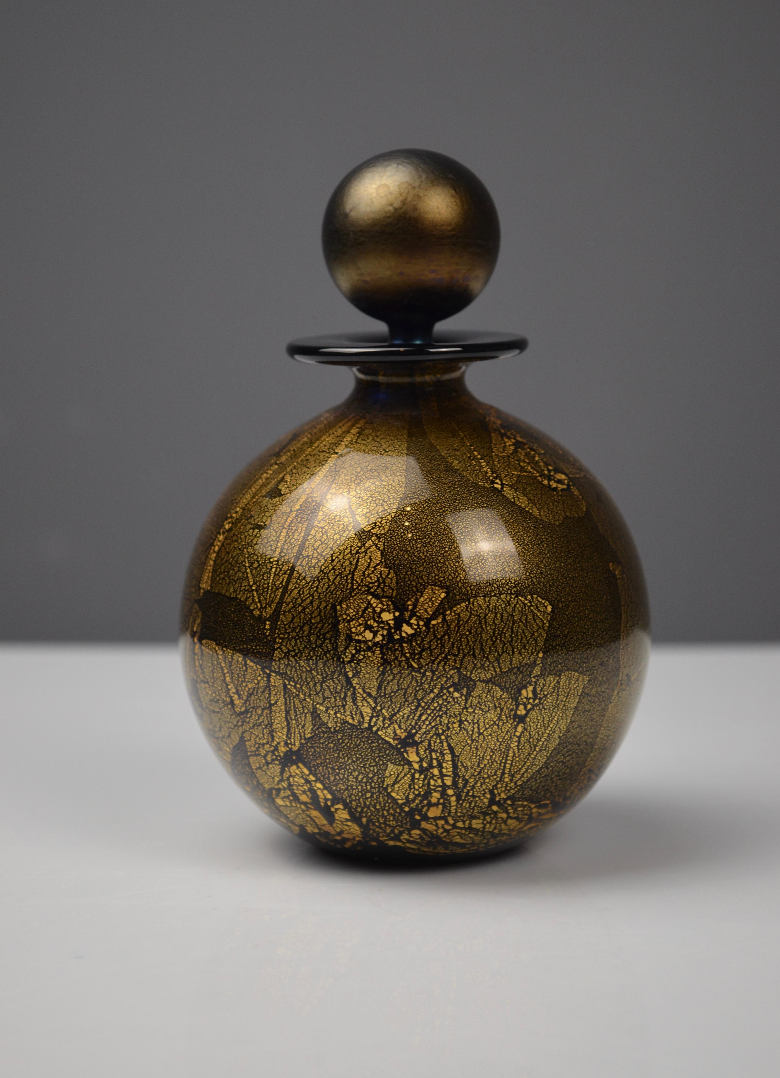 Bellissima bottiglia di profumo in vetro soffiato firmata Isle of Wight Studio Glass.
Il suo corpo sferico presenta una sorprendente decorazione iridescente dorata e nera con un caratteristico effetto crepato. Il tappo sferico dorato aggiunge