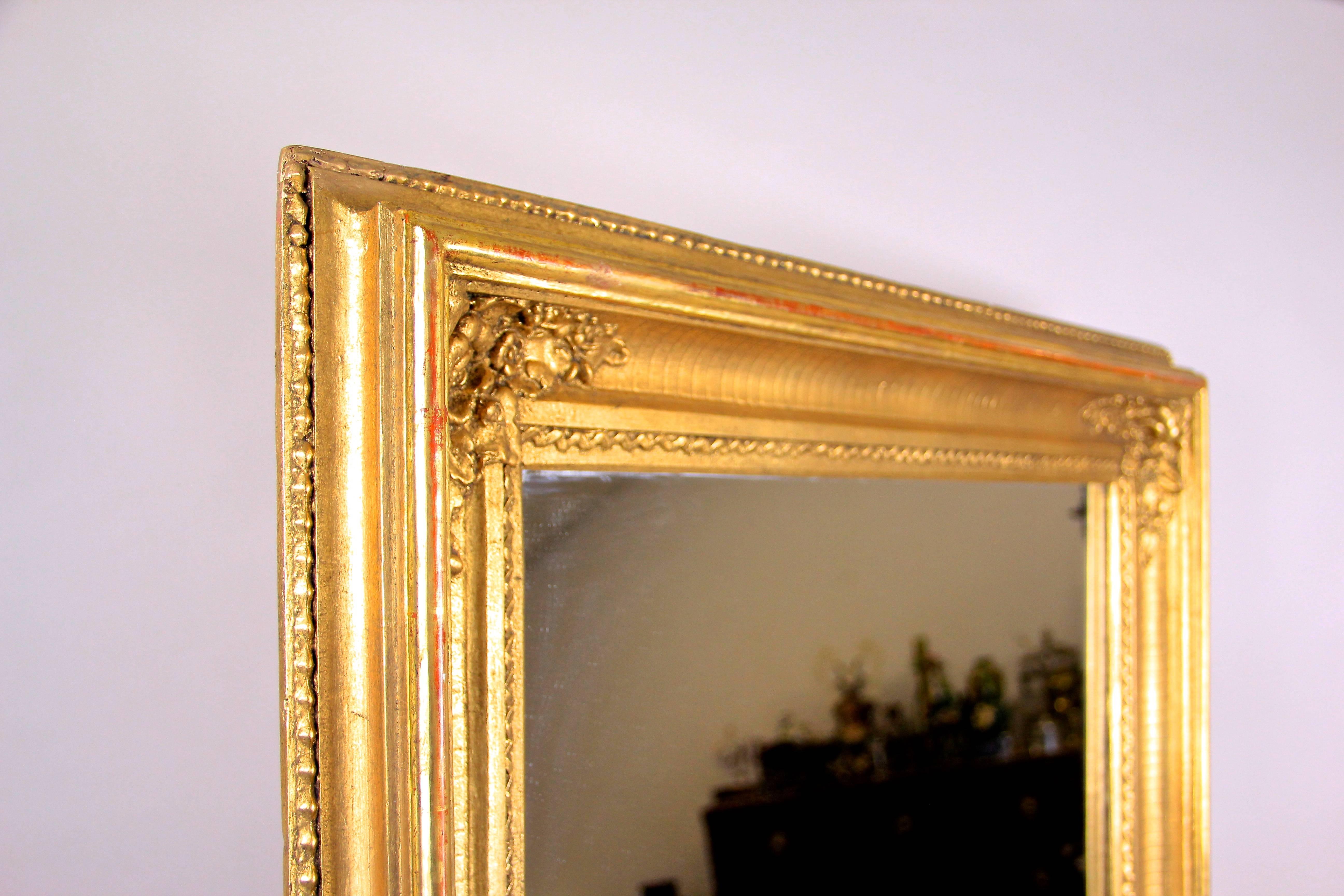 Beautiful golden Biedermeier wall mirror out of Austria dating back to circa 1850. The precious surface shows extensive gilt techniques and artfully processed floral stucco motifs in each corner. The gold leaf covered outer strip show the red