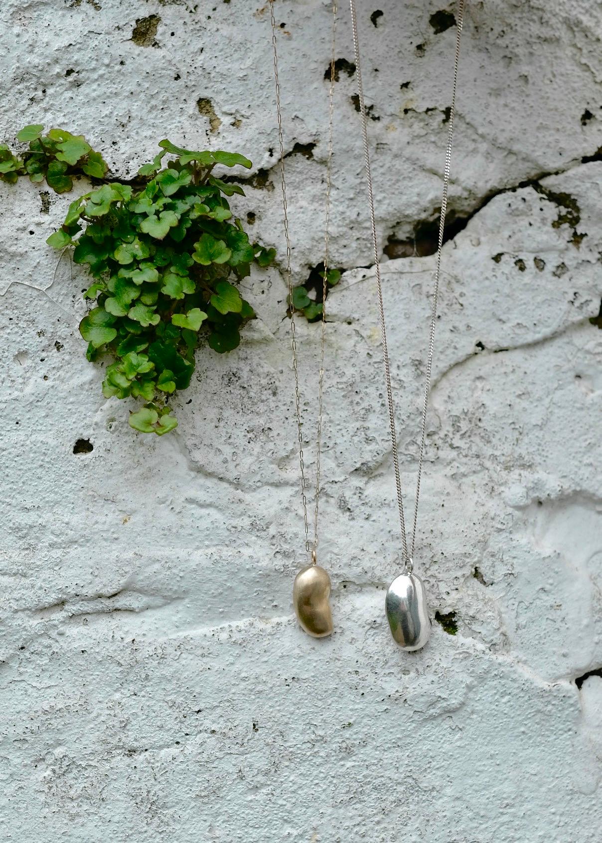 This pendant is elegantly shaped with a playful twist. 

It is cast from a real kidney bean in golden brass, and is  finished with a matte sheen to subtly catch the light when worn. No two are the same. 

The 16-18