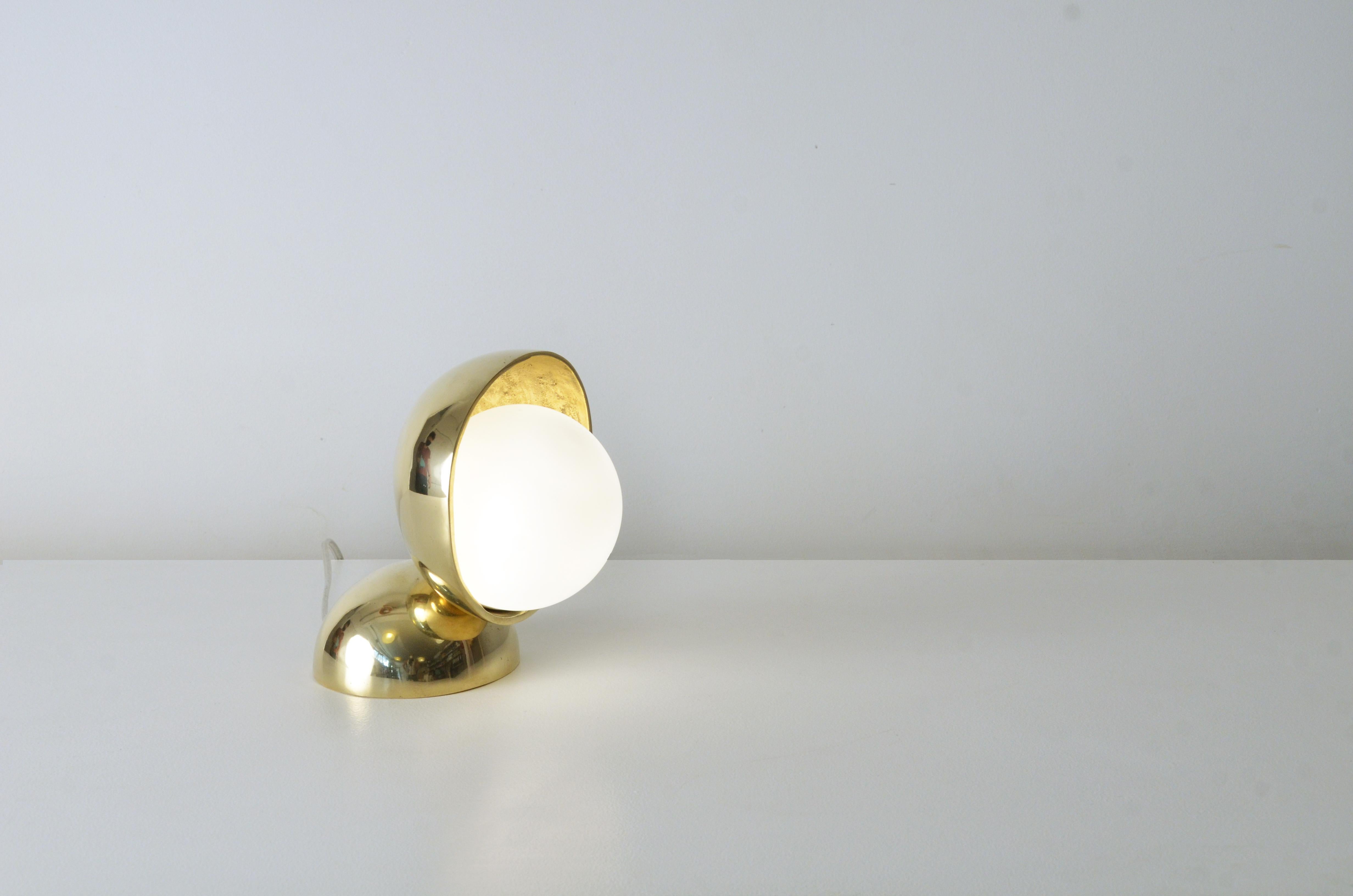 Cette lampe de table contemporaine dorée est une petite pièce entièrement réalisée en bronze coulé avec un verre de lait au milieu. La lampe (G9) se trouve à l'intérieur de ce verre rond et laiteux, qui transforme la lumière émise par la lampe en un