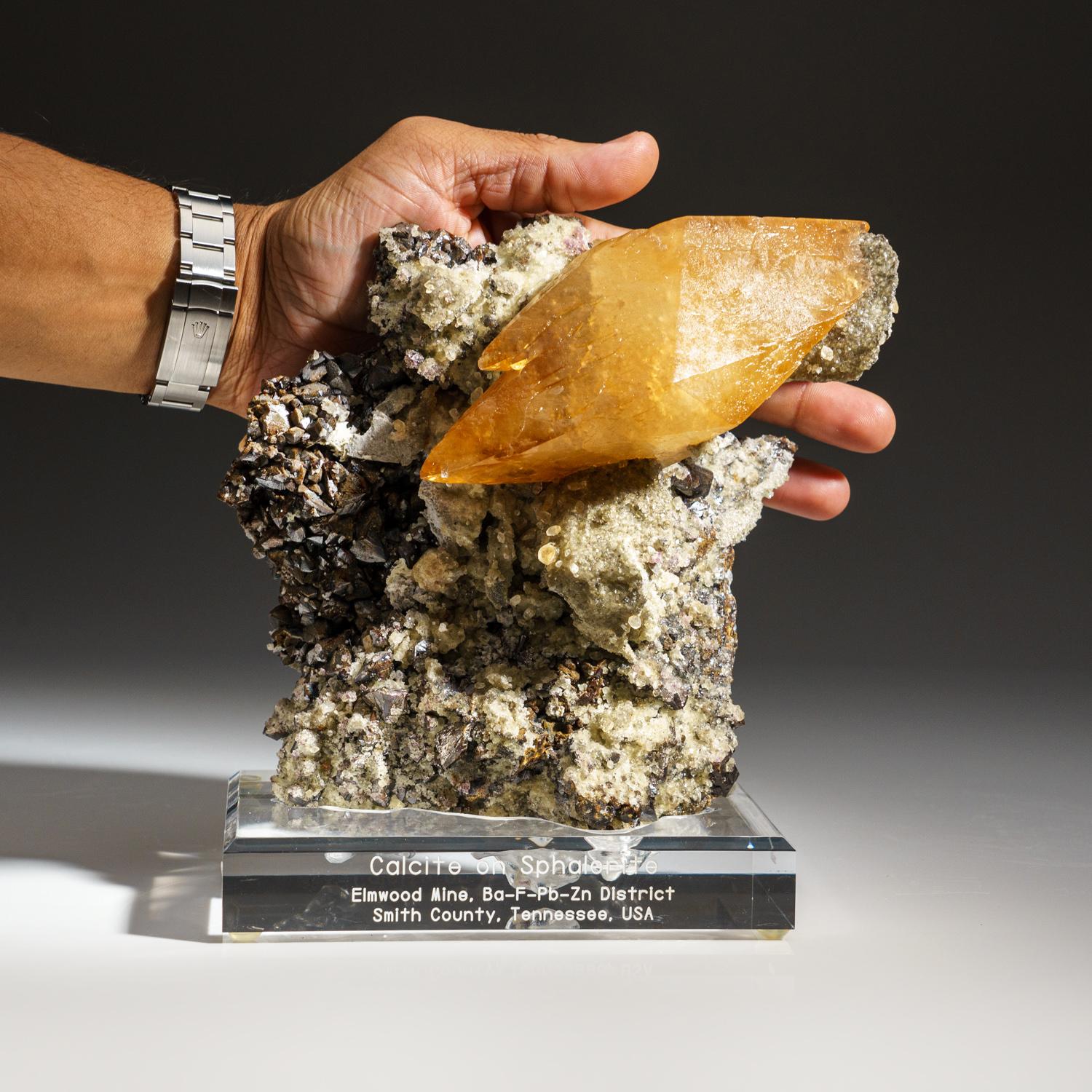 From Elmwood Mine, Tennessee, United States.

Large, museum-quality, lustrous transparent deep golden calcite with sphalerite crystal at the base of the crystal. Double terminated scalenohedral twinned on the C-axis with well defined re-entrant