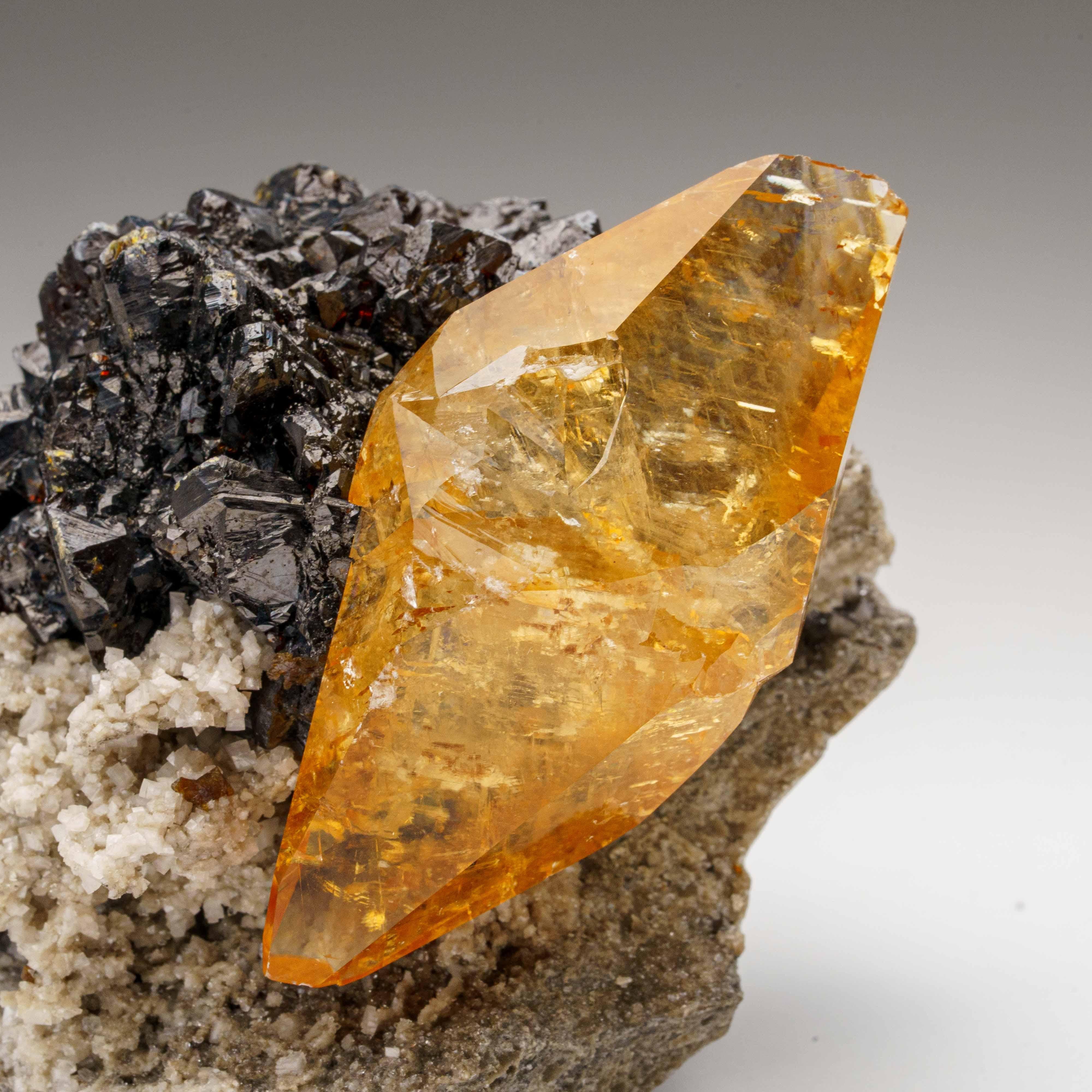 Aus der Elmwood Mine, Tennessee, Vereinigte Staaten.

Großer, glänzender, transparenter, tiefgoldener Calcit in Museumsqualität mit Sphaleritkristall an der Basis des Kristalls. Doppelt endständige, auf der C-Achse verzwillingte Skalenoeder mit gut