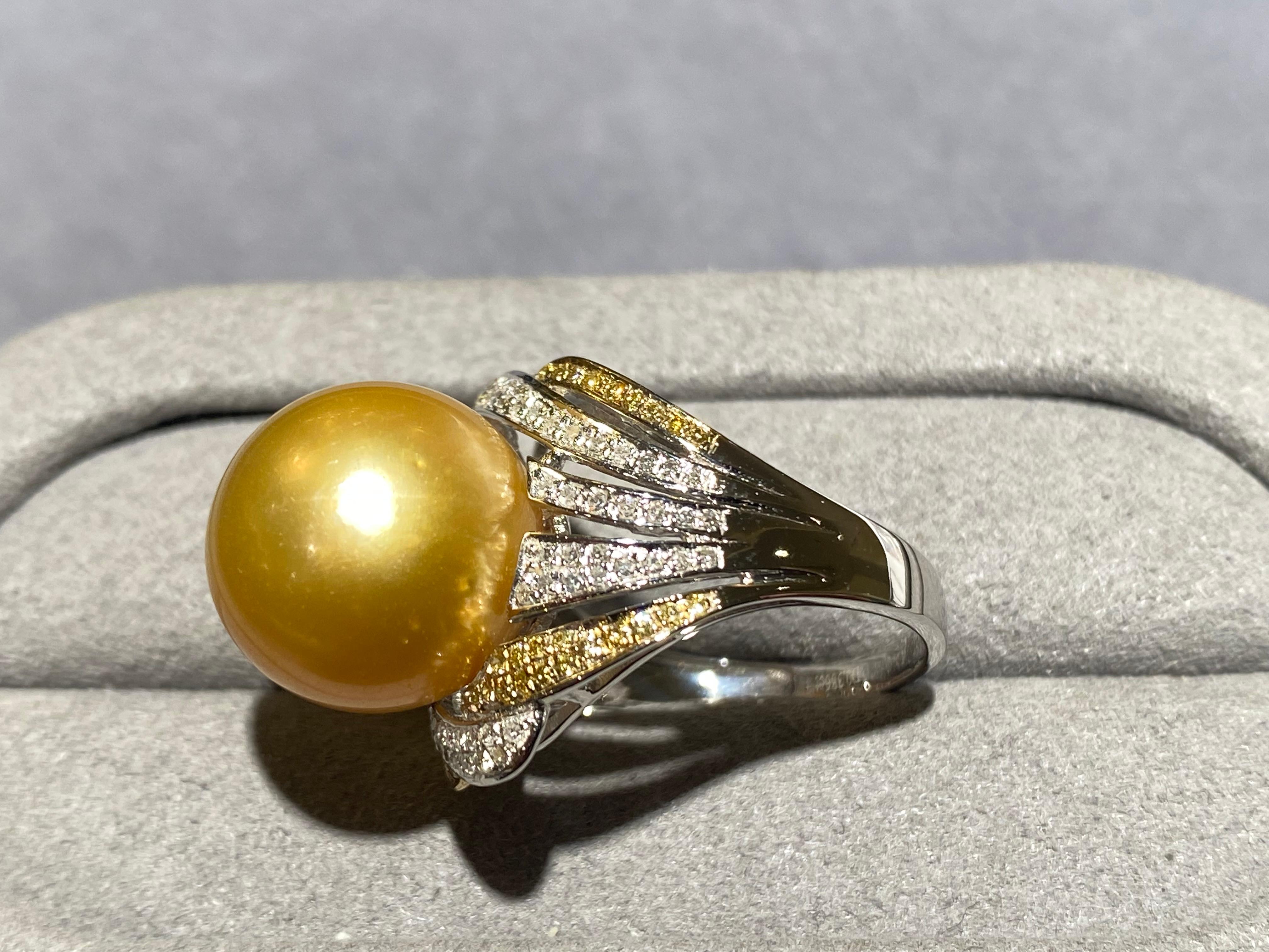 A round  13.5 mm golden colour south sea pearl and diamond ring in 18k white gold. The ring band underneath the south sea pearl is ribbon-like and set with diamond pave. The ribbons are alternating between yellow and white colour. This ring is