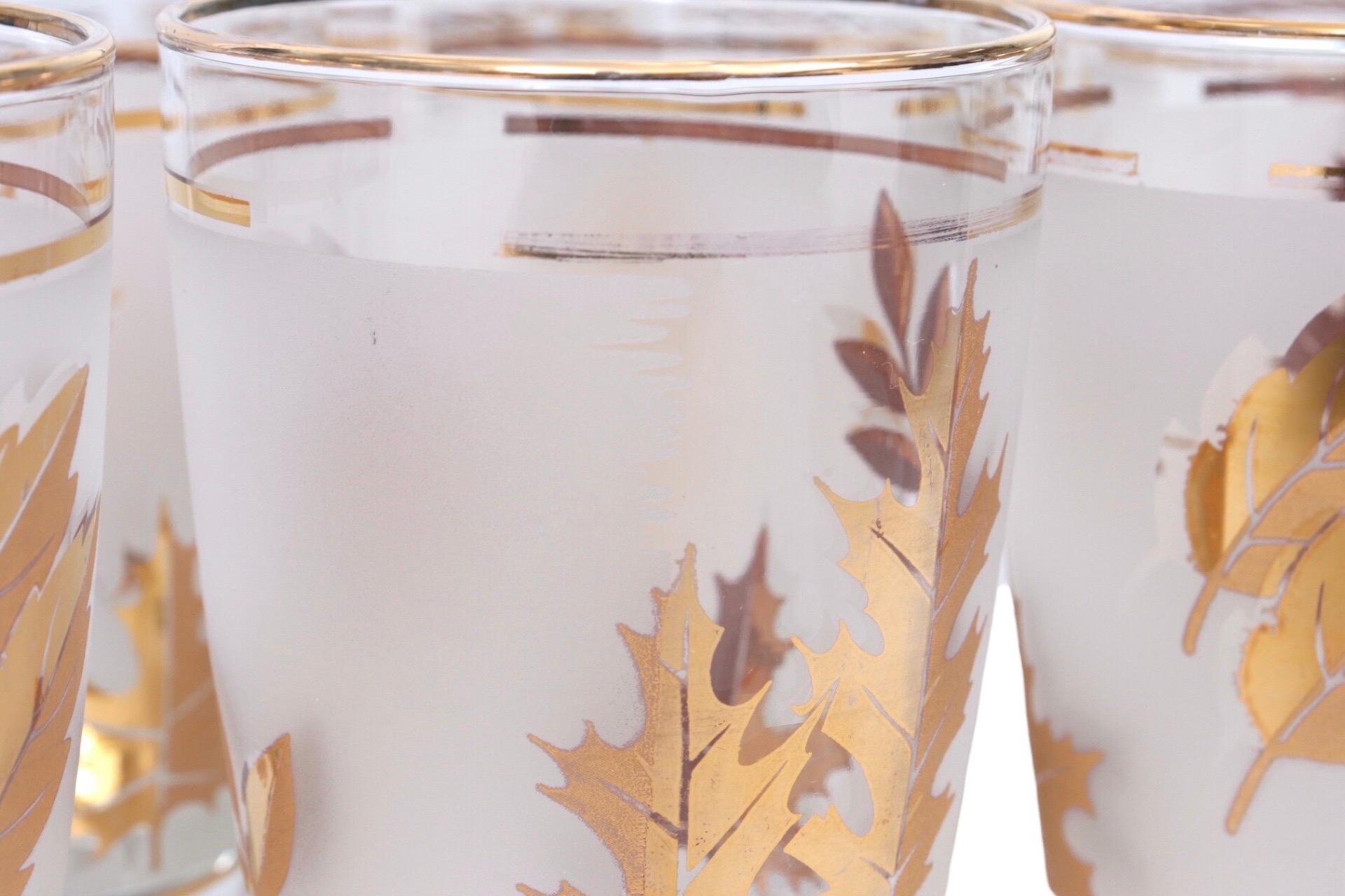 A set of ten 'Golden Foliage' tumblers by Libbey Glass Company. Tall glasses are decorated with gilt leaves against a band of frosted glass, trimmed with a thin gilt line. Glasses are marked underneath with a cursive ‘L’ attributed to Libbey Glass