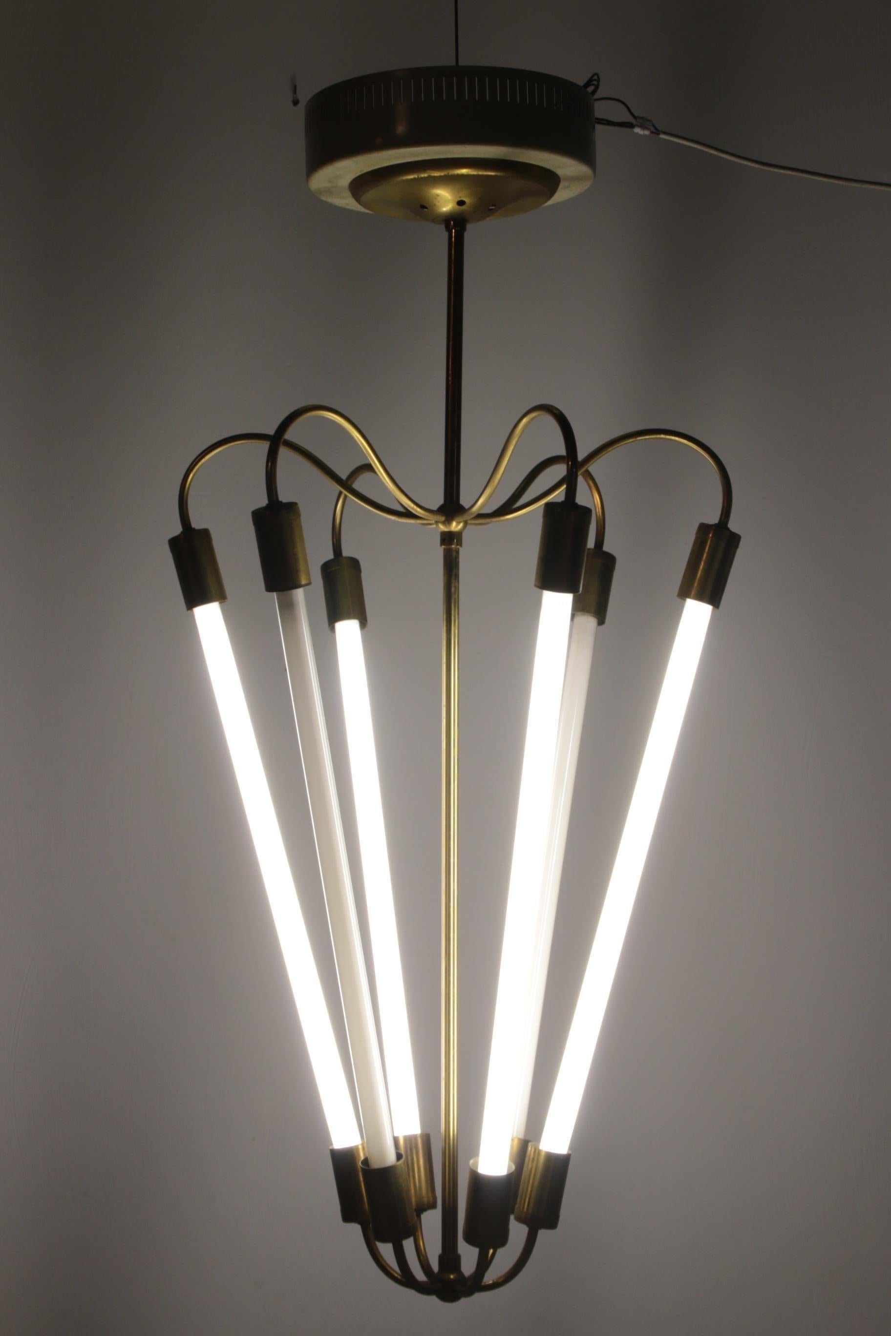This Art Deco inspired Bauhaus chandelier has a gold coloured brass frame in which there is space for 6 fluorescent lights. 
The design is by the German creator Christian Dell for the brand Kaiser & Co. The ceiling mount is also made of metal and