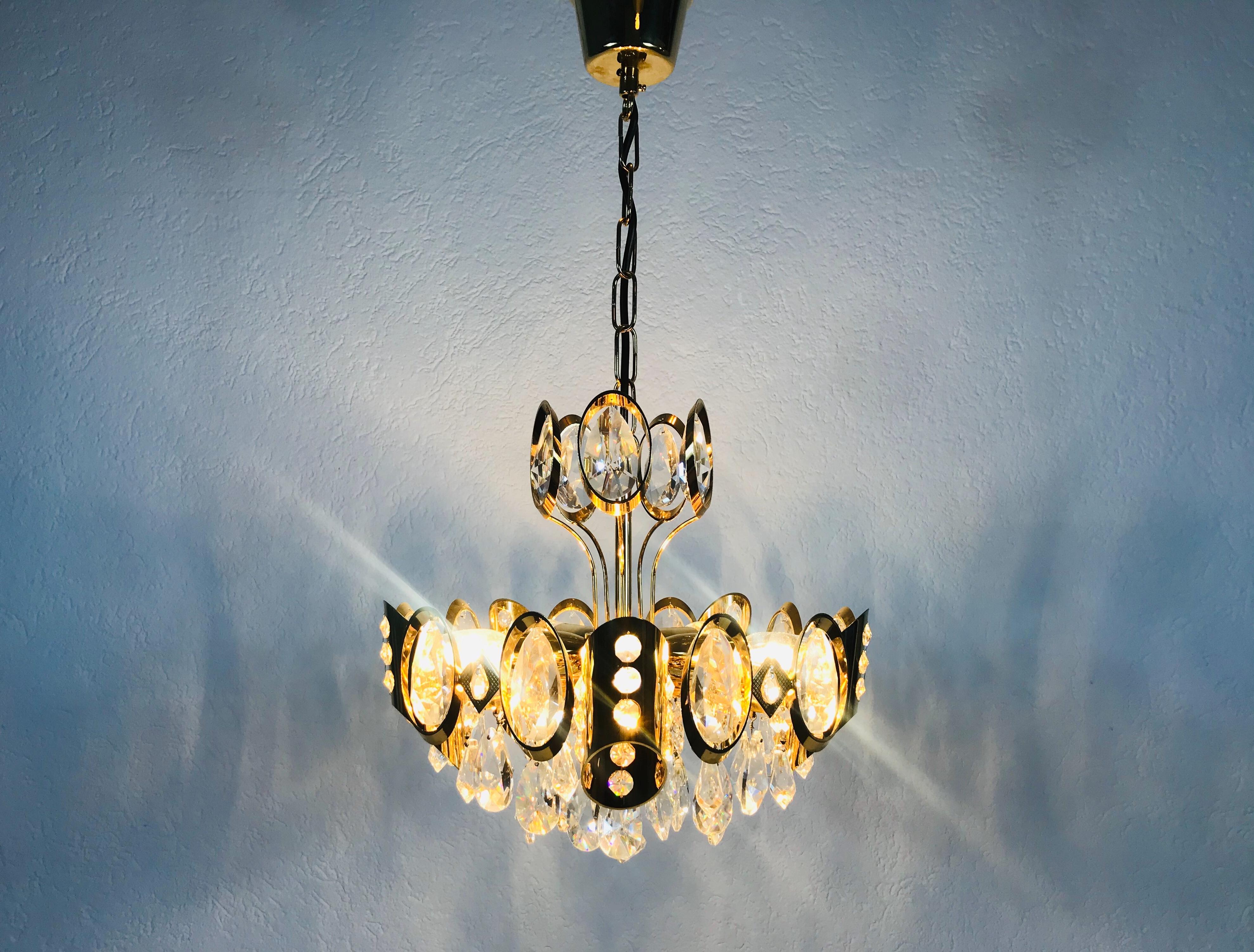 Un lustre extraordinaire de Palwa, fabriqué en Allemagne dans les années 1960. La lampe a un design très élégant. Il est réalisé dans la période de Hollywood Regency. Corps rond en laiton doré avec cinq prises E14. Le corps est entouré de cristaux