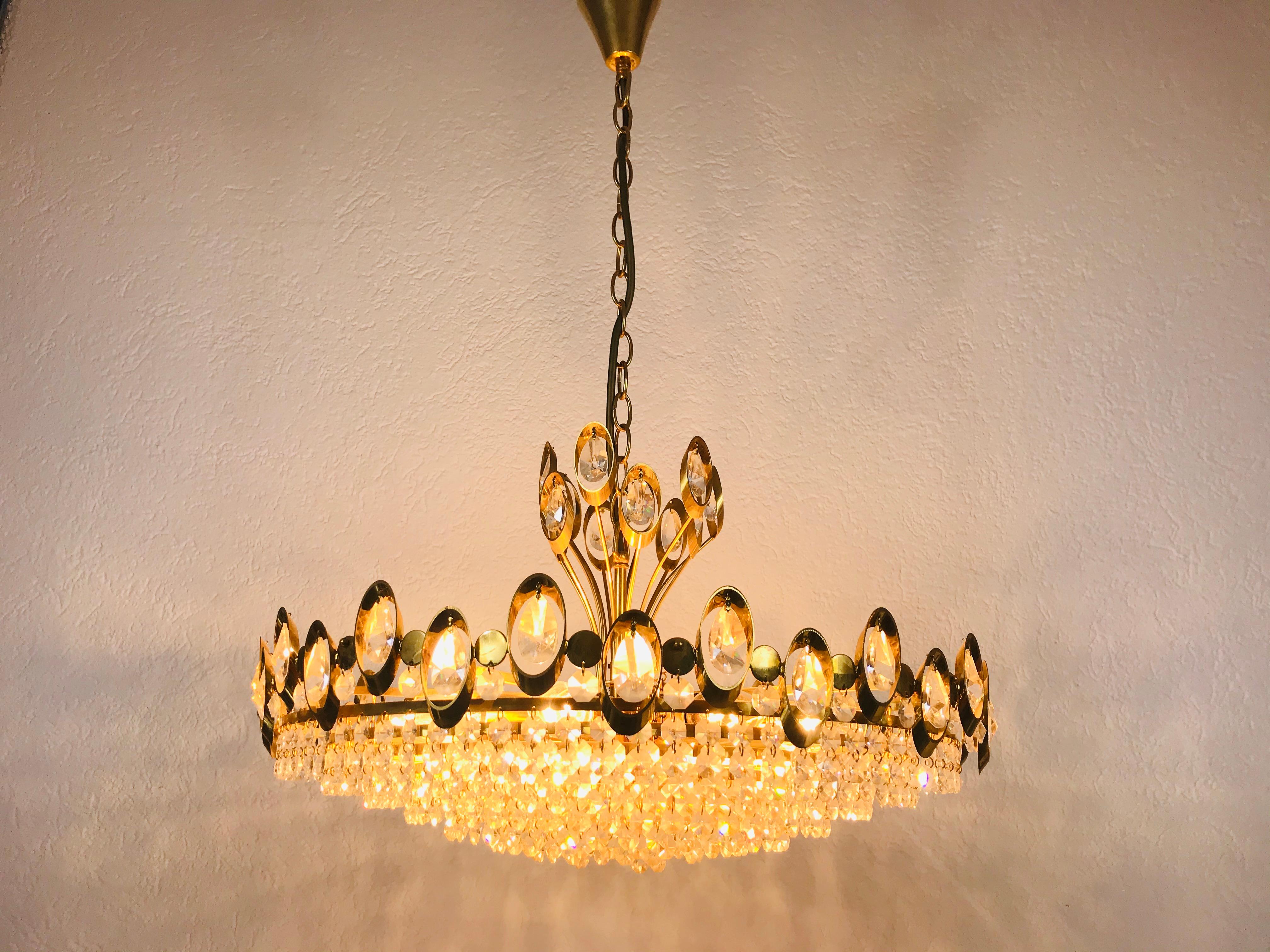 Un lustre extraordinaire de Palwa, fabriqué en Allemagne dans les années 1960. La lampe a un design très élégant. Il est réalisé dans la période de Hollywood Regency. Corps rond en laiton doré avec douilles E14. Le corps est entouré de cristaux très