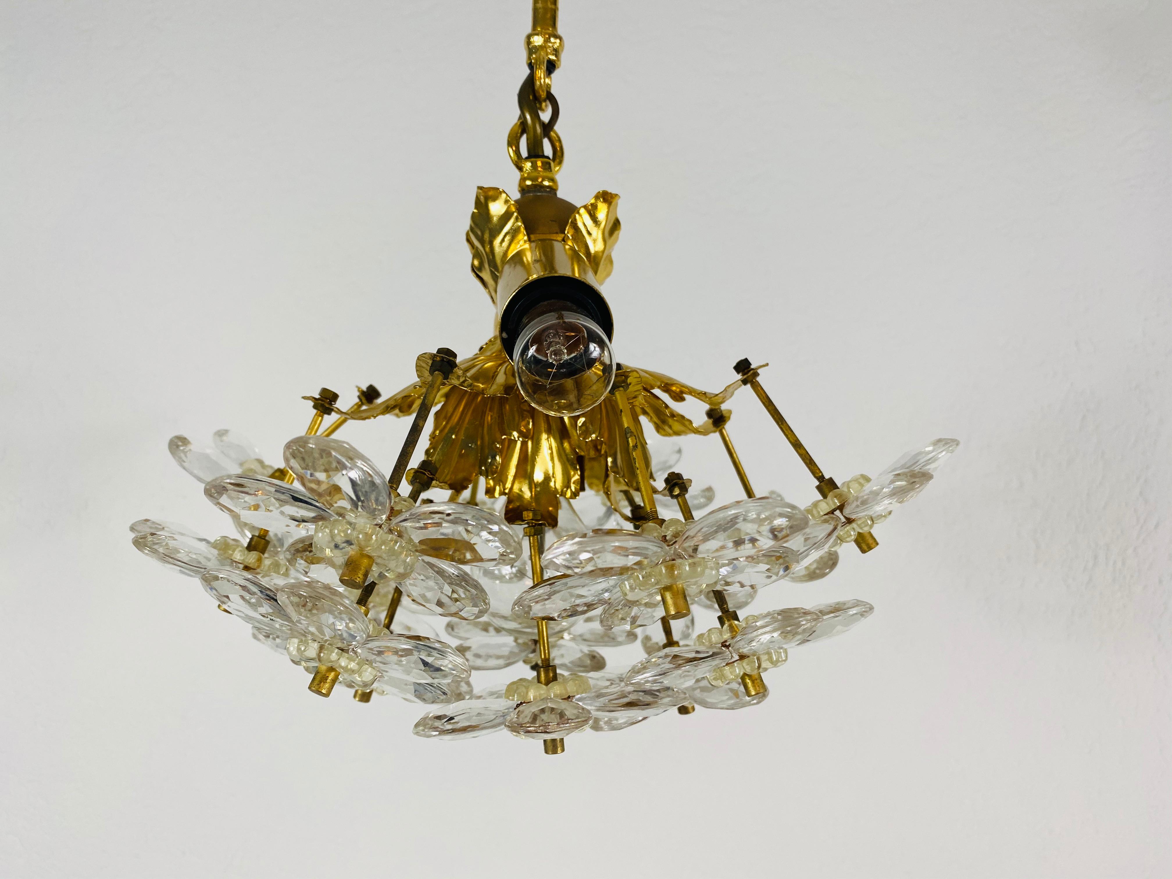 Un lustre extraordinaire de Palwa, fabriqué en Allemagne dans les années 1960. La lampe a un design très élégant. Il est réalisé dans la période de Hollywood Regency. Corps rond en laiton doré avec douilles E14. Le corps est entouré de cristaux très
