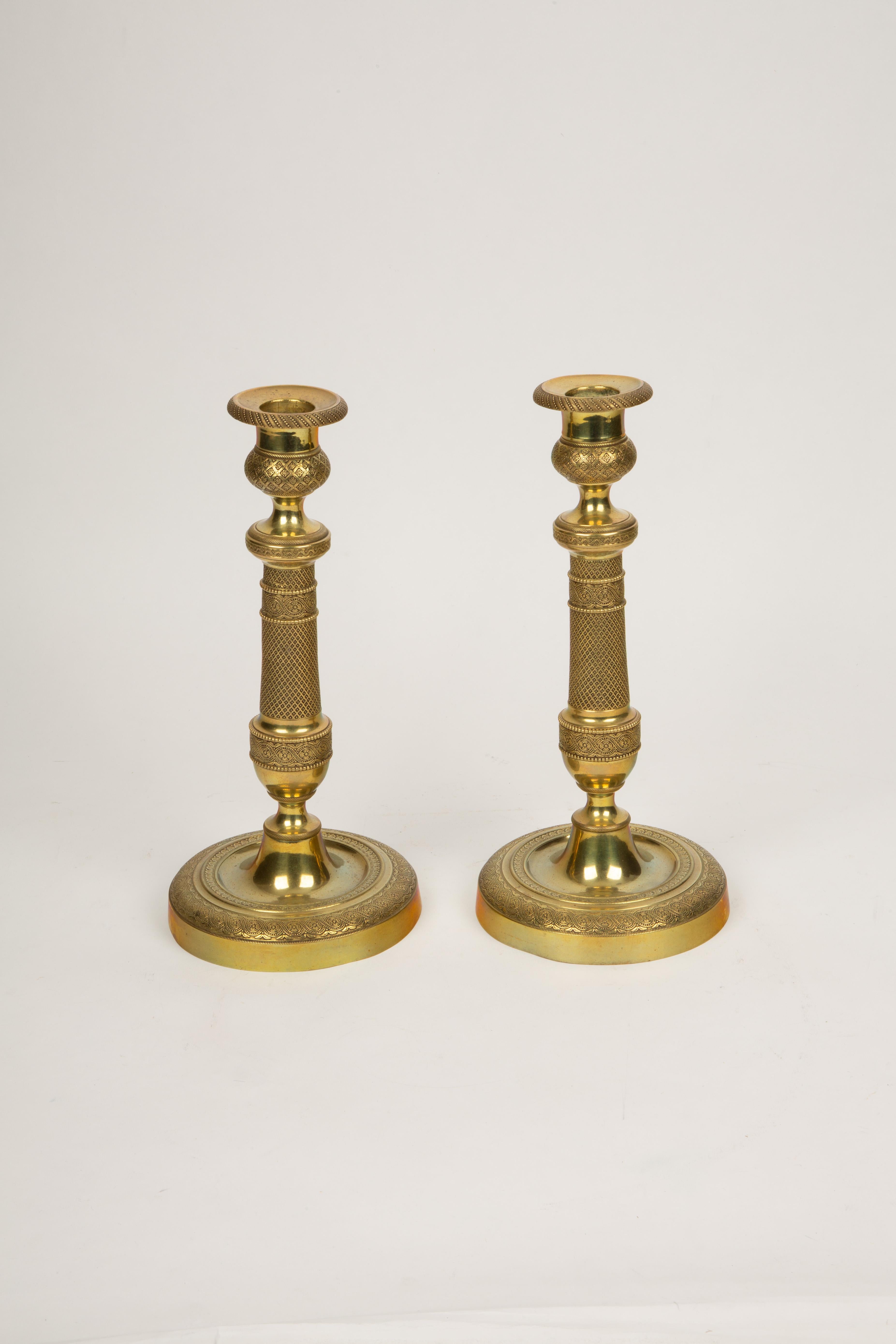 An exquisite pair of French Restoration period gilt bronze candlesticks, dating to the early 19th century (circa 1820), showcasing exceptional craftsmanship and intricate detailing. These elegant candlesticks are distinguished by their refined