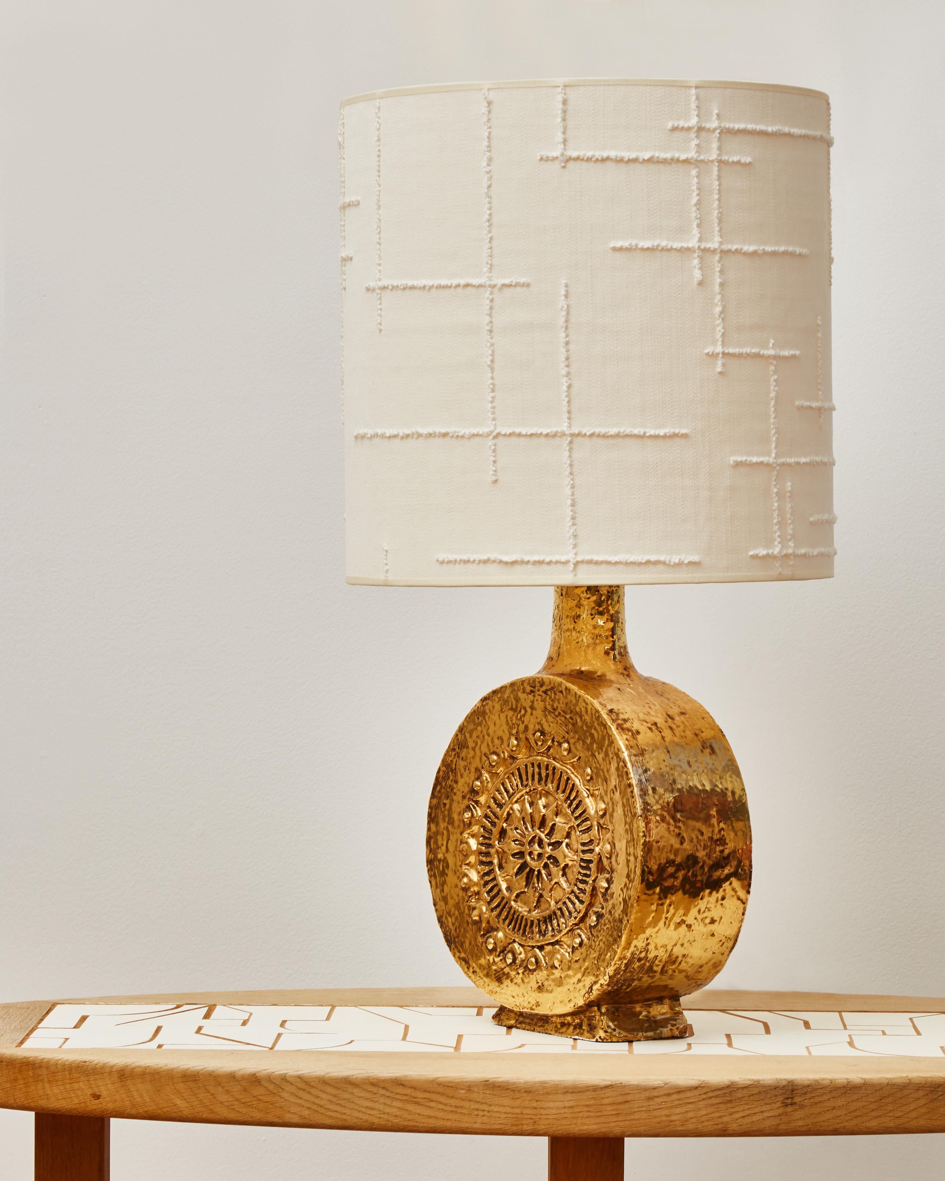 Decorative ceramic table lamp glazed with a beautiful gold layer beautifully reflecting the light. Topped here with a new lampshade made of Dedar fabric.