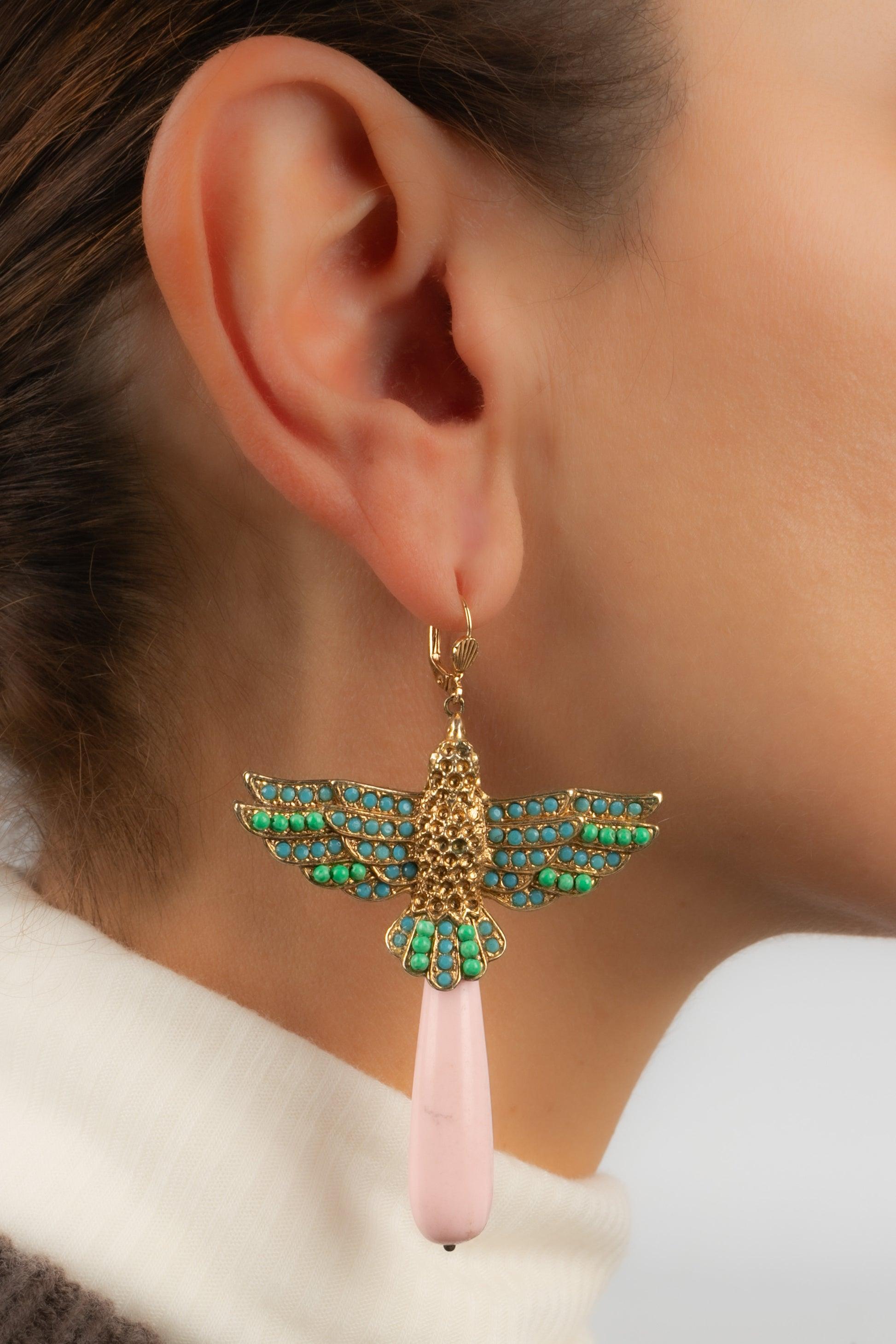 Golden metal earrings representing a bird ornamented with blue rhinestones, green glass pearls, and holding a pink glass paste drop.

Additional information:
Condition: Very good condition
Dimensions: Height: 7.5 cm

Seller Reference: BO218