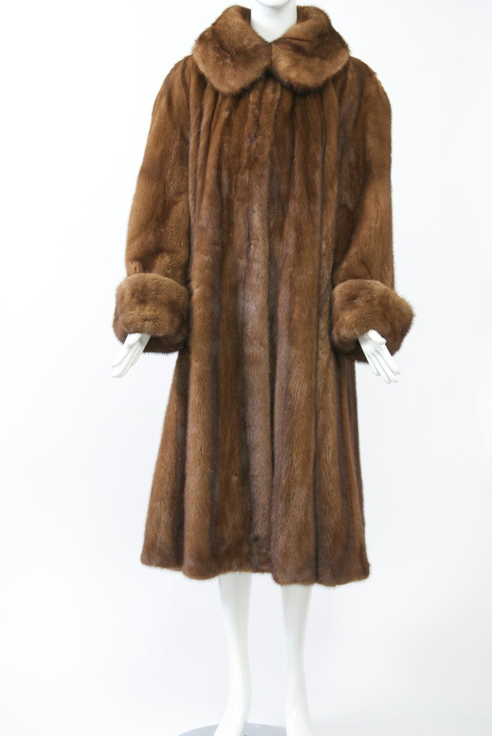 Wrap yourself in luxury and warmth with this golden mink swing coat. Ample vertical skins boast a round collar, dolman sleeves and deep, turned back cuffs. Hidden slash pockets. Decorative button at neck, two fur hook closures in front. A glamorous