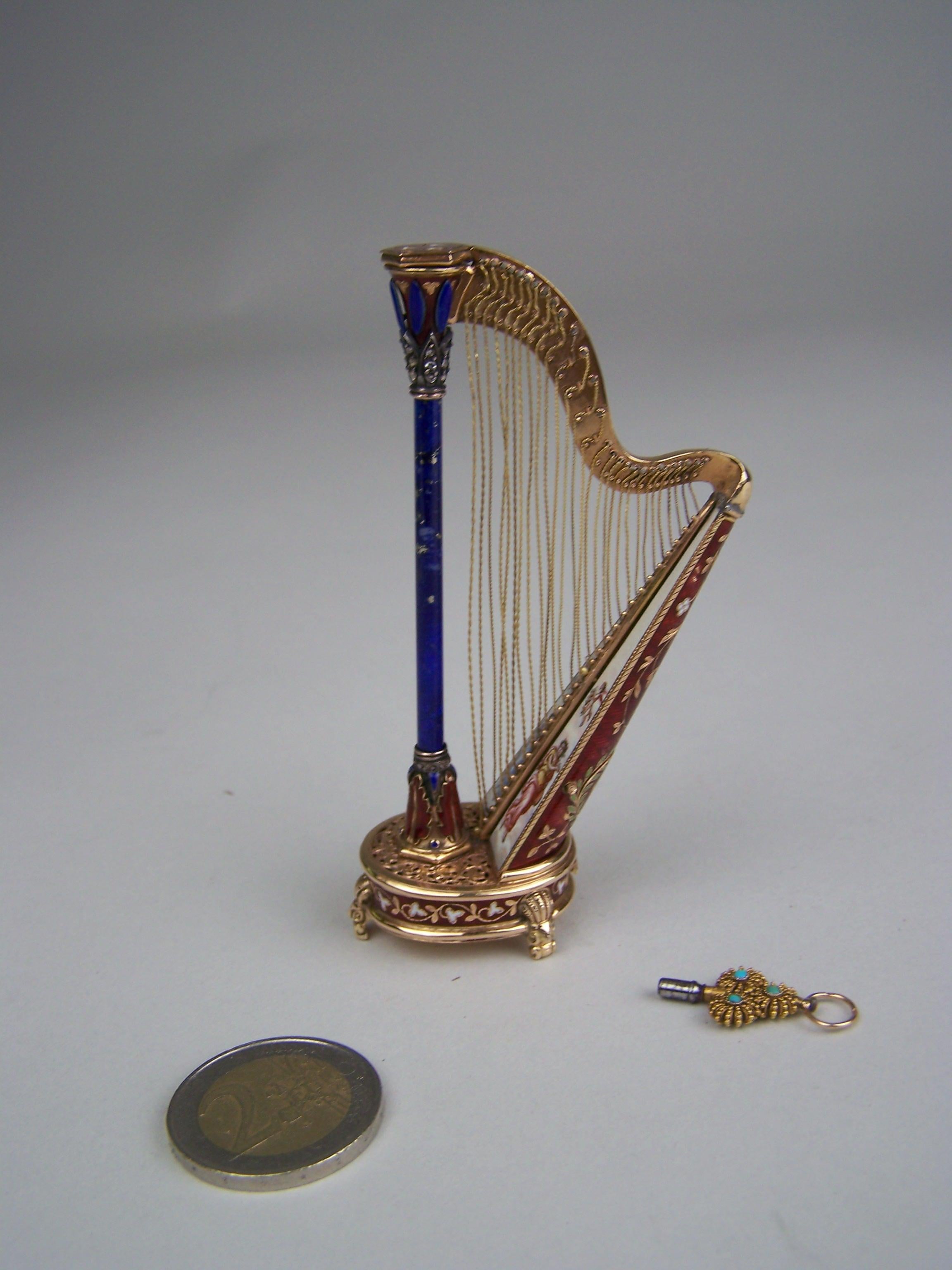 Very rare golden (14K) musical harp with barilet movement to the bottom.
case made by Köchert AE

Mechanism raised on 3 golden feed and having red transludent enamel to the side. Champleve with white leaves. The top of the musical case finished with