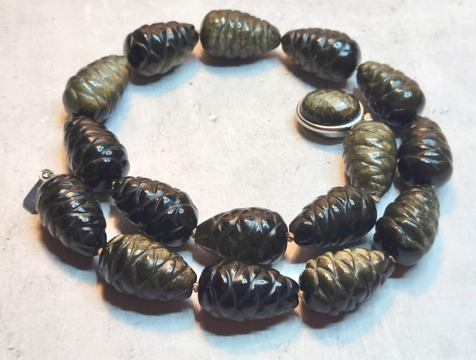 La collana è lunga 44,5 cm e le perle intagliate misurano circa 25,5 x 15,5 mm. Ogni perlina è sapientemente intagliata a forma di pigna. Un lavoro straordinario!
L'ossidiana Golden Sheen è un'ossidiana di colore marrone e nero che riflette una
