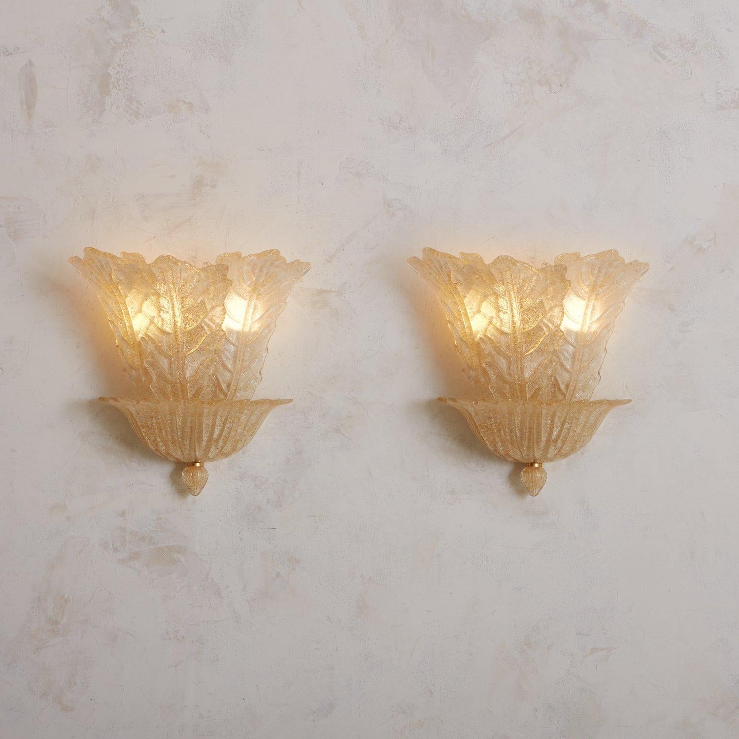 A vintage hand blown Murano glass sconce in an opalescent peach hue with beautiful, realistic textural details. This sconce has three leaf motifs which sprout from a flared demilune base with a bottom finial and brass detail. Sourced in Italy,