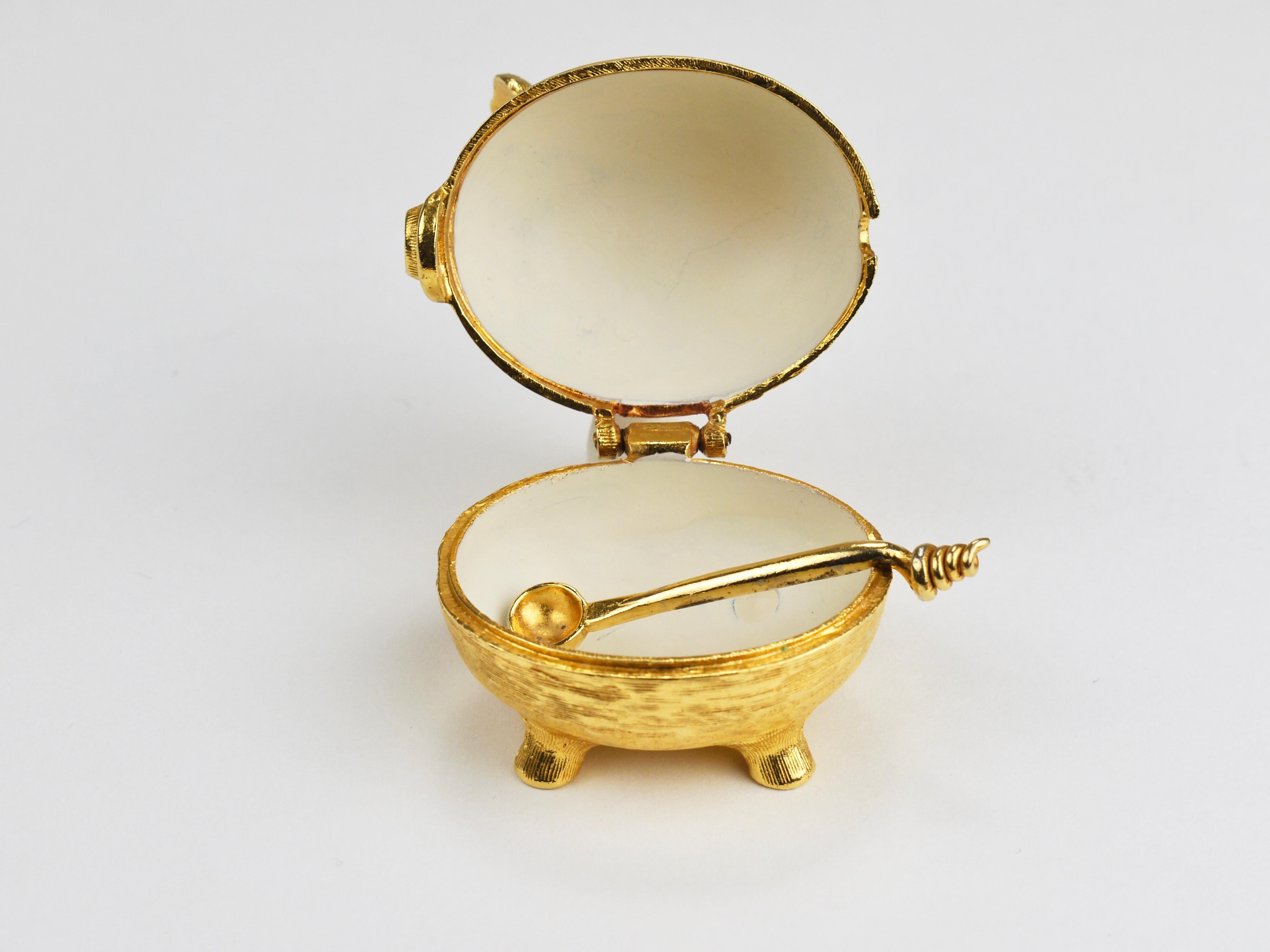 This is a cute, tiny pig made of fire-gilded gilt metal from the 1970s — a quirky little object in the shape of a piglet. It’s a small container with a hinged lid, a white enameled interior, and a little spoon. A charming detail: the handle of the
