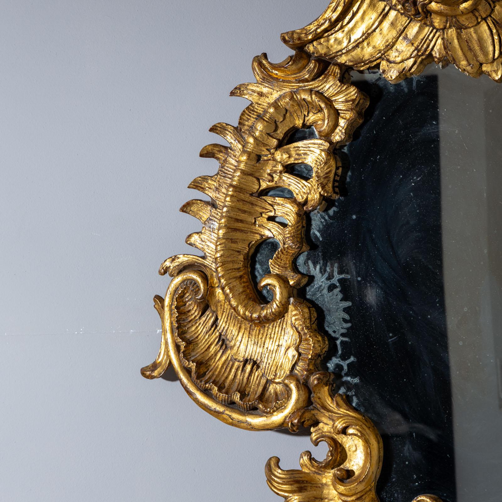 Large Rococo wall mirror in a gold-patinated, curved frame with rocailles and shell ornaments as well as a winged putto head as a crown. Red wax seal on the reverse of the Prince Salm-Kyrburg (illegible): “Hoch. Fürst Salm-Kyrburg  Marschall Amts