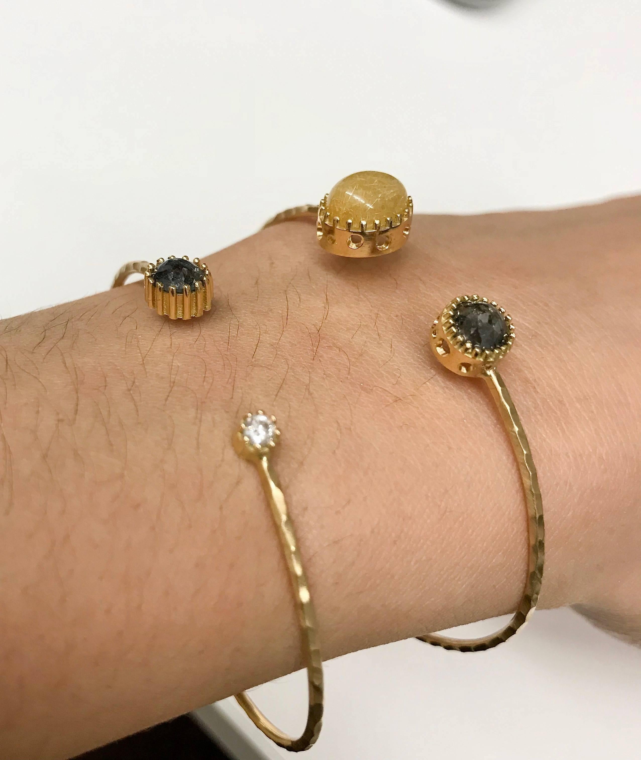 Open cuff with a round rose cut natural-colored black diamond and oval cabochon golden rutilated quartz. The raised settings compliment the stone's shape, exaggerating their height subtly. Oculus openings dotting the exterior of the settings can