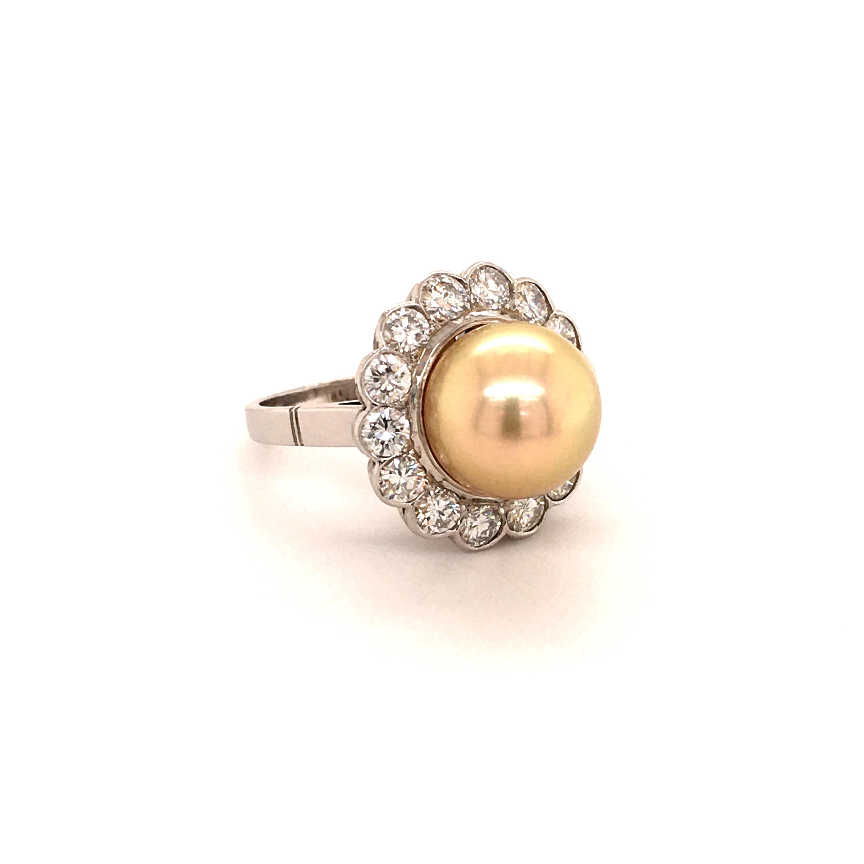 This elegant ring in 14 karat white gold features a beautiful gold colored, round South Sea cultured pearl of 12.0 mm in diameter. The surface of the pearl is clean with an excellent luster. Surrounded by 14 brilliant cut diamonds of G/H color and