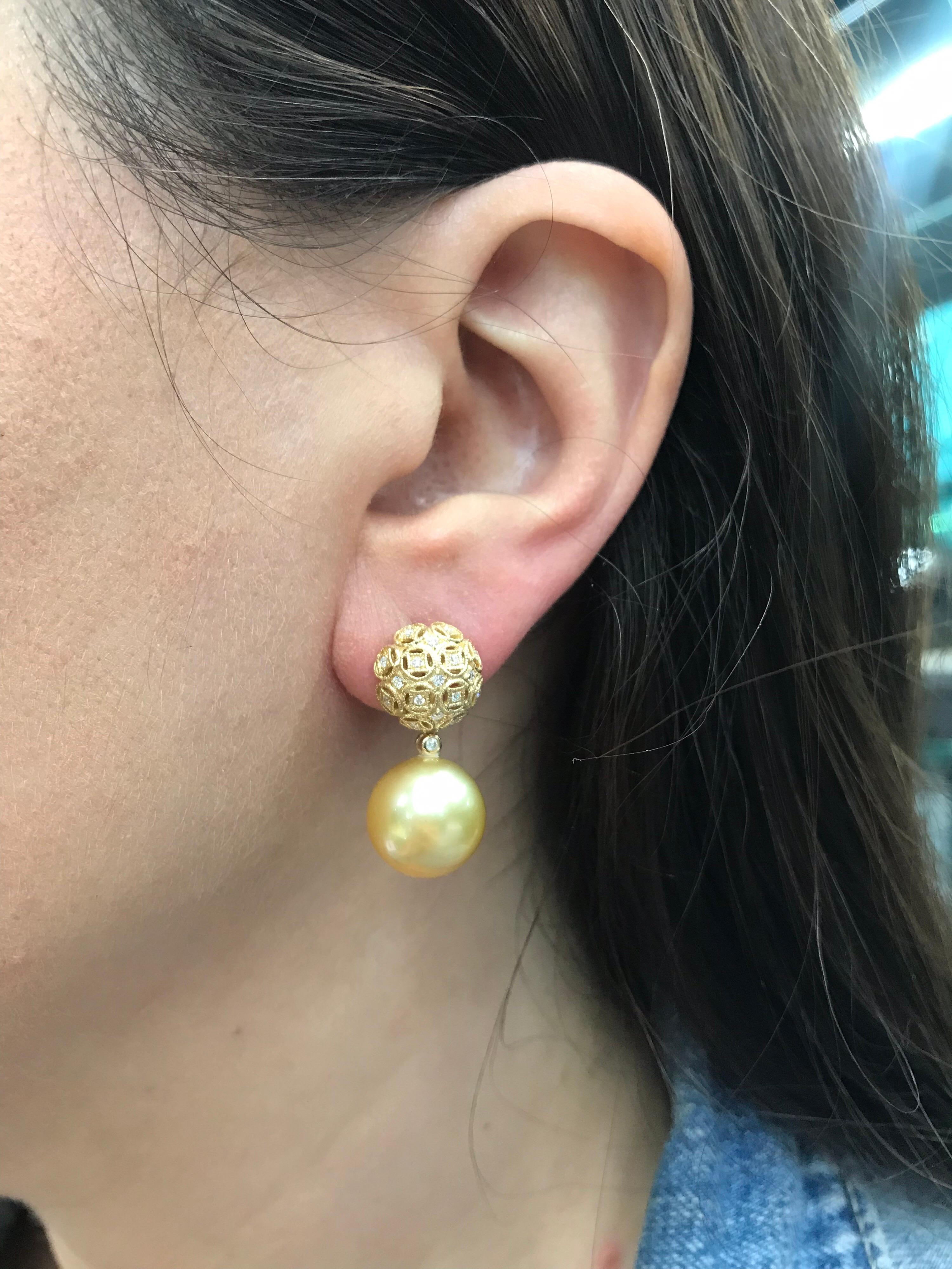 18K Yellow gold drop earrings featuring two Gold South Sea pearls measuring 13-14 mm flanked with round brilliants weighing 0.30 carats. 