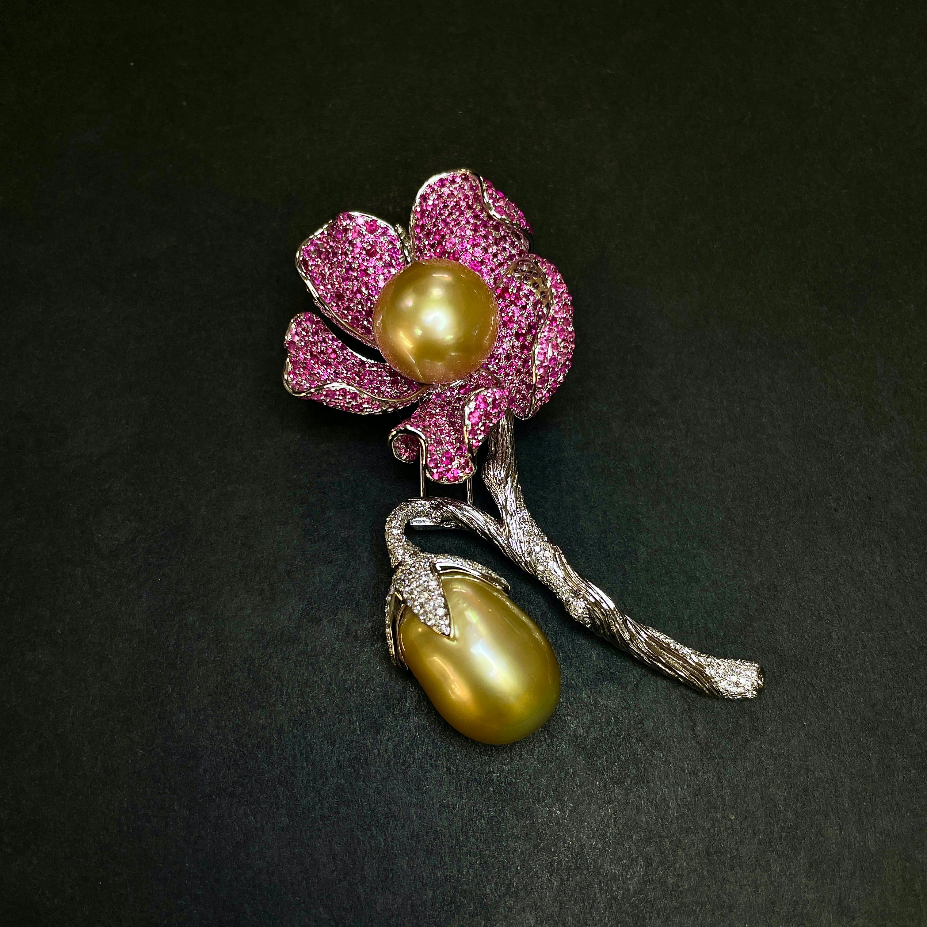 Eine fruchtige und blühende Brosche mit goldener Südseeperle, rosafarbenem Saphir und Diamantbesatz. Die runde goldene Südseeperle ist von 5 mit rosa Saphiren besetzten Blütenblättern umgeben, während sich die Frucht vom Hauptstamm, auf dem die