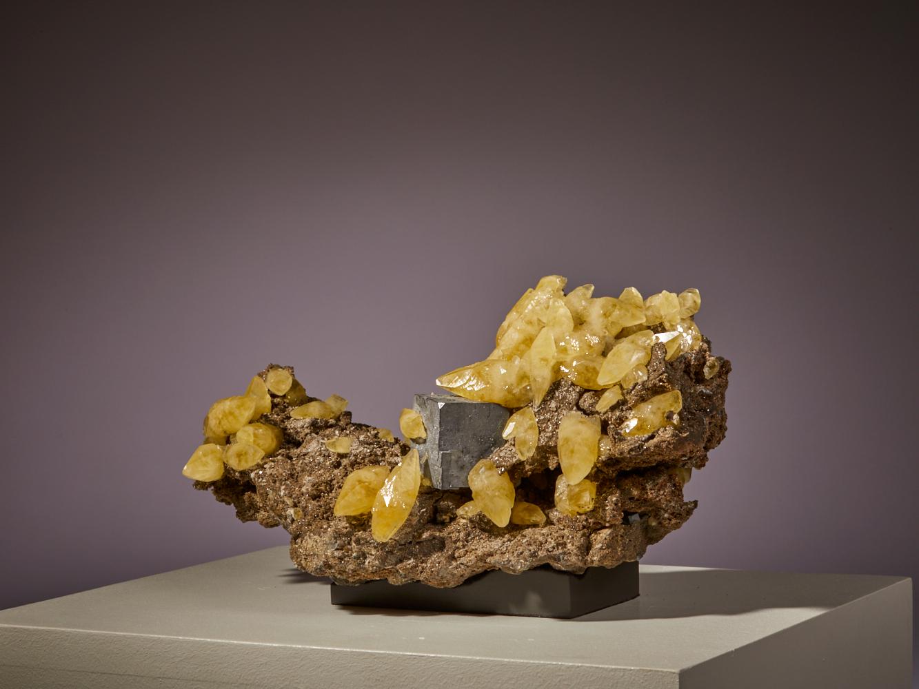 Regálate la vista con este extraordinario ejemplar de vibrantes cristales de calcita amarilla, elegantemente posados sobre una matriz natural, procedente de los ricos yacimientos minerales de EE.UU. Los llamativos tonos dorados de la calcita crean