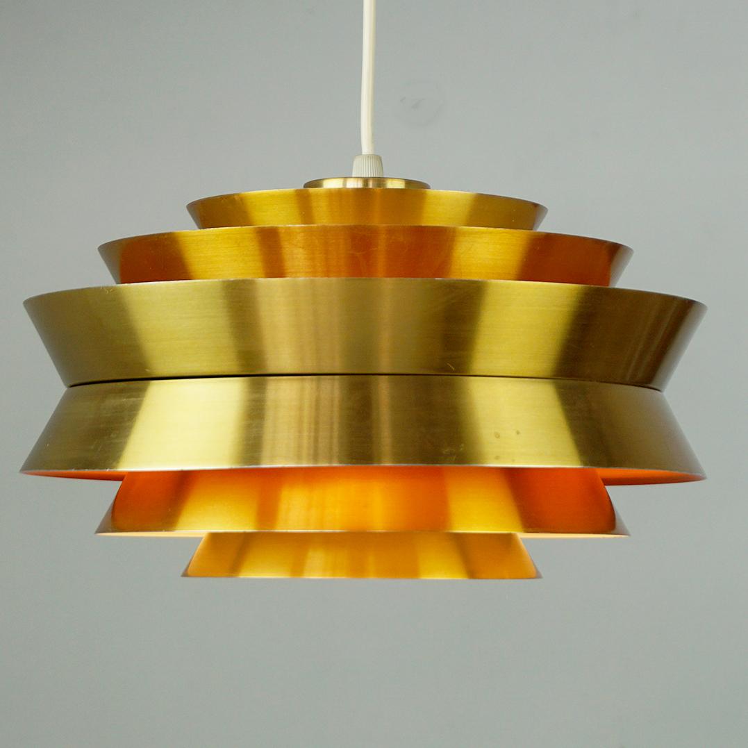 This Scandinavian Modern brass colour aluminium trava pendant  was designed by Carl Thore alias Sigurd Lindquist and Manufactured at Granhaga Metal Industri in Sweden during the late 1960s. It features a tiered construction with different angled