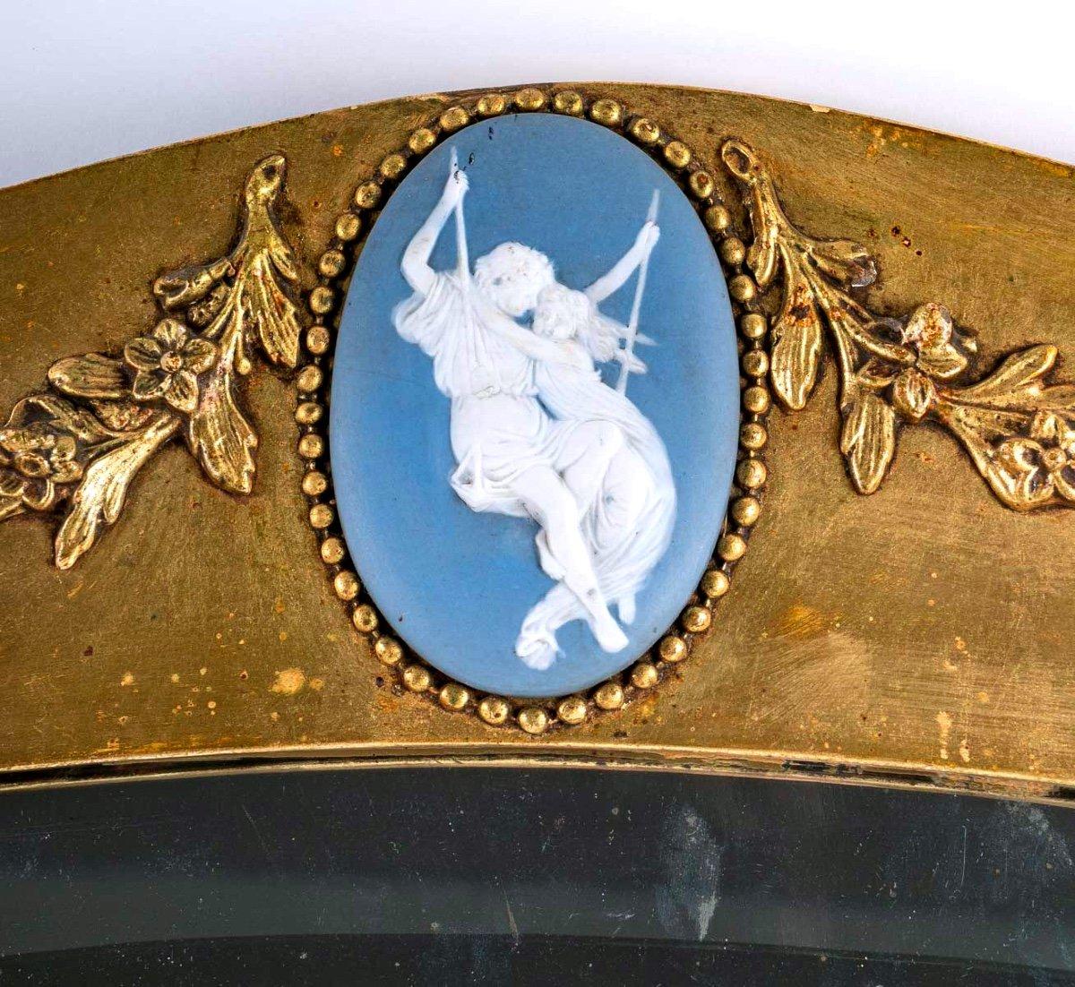 Lovely oval-shaped giltwood mirror. Its original glass is bevelled.
Its pediment decorated with floral garlands reveals in its center a delicious blue jasper Wedgwood porcelain medallion representing a young biscuit couple, seated on a swing