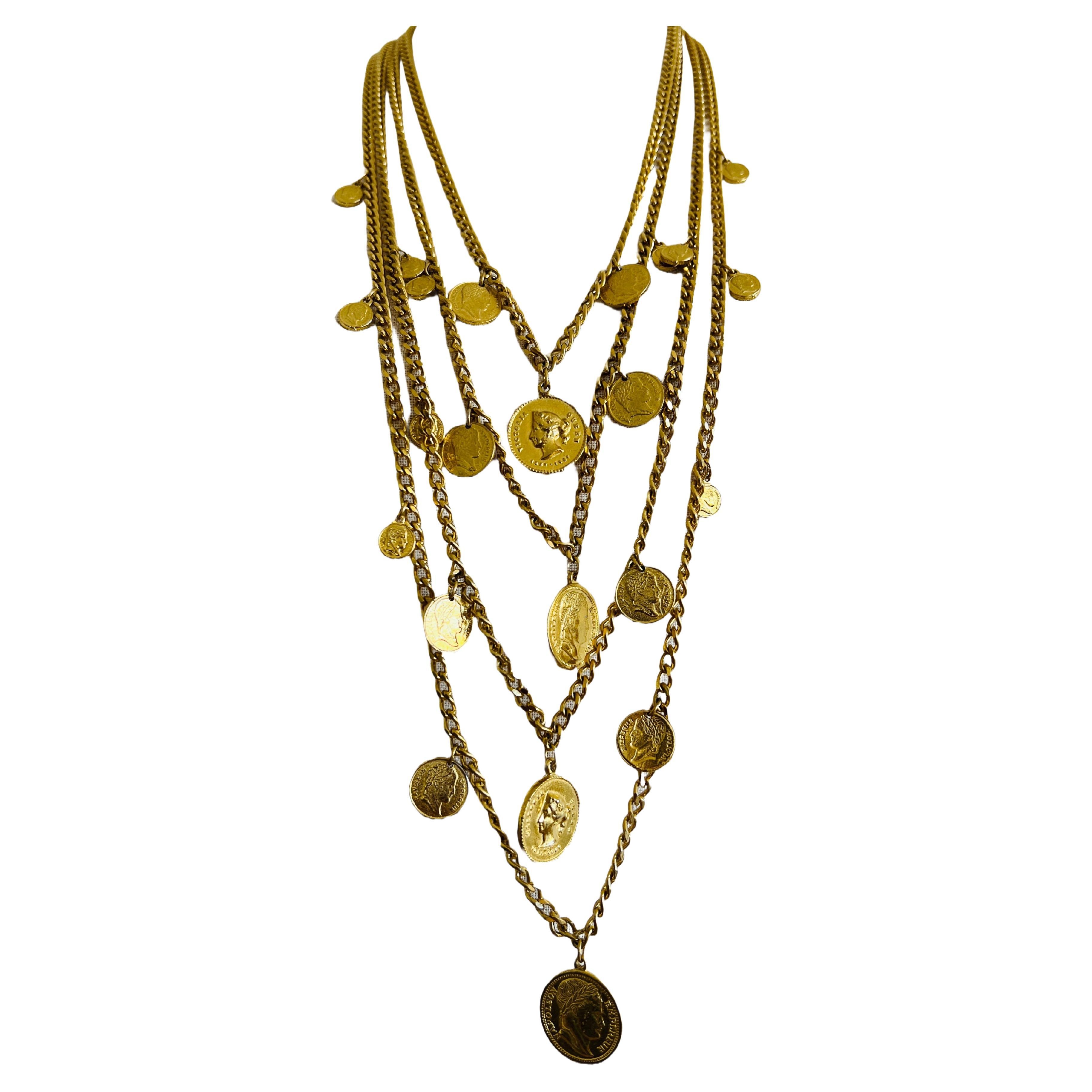 Diese stilvolle Halskette ist ein echtes Statement: Sie besteht aus mehreren Strängen goldfarbener Ketten, die jeweils mit aufwändig gestalteten Münzmedaillons verziert sind. Die Münzen sind klassischen und mittelalterlichen Designs nachempfunden