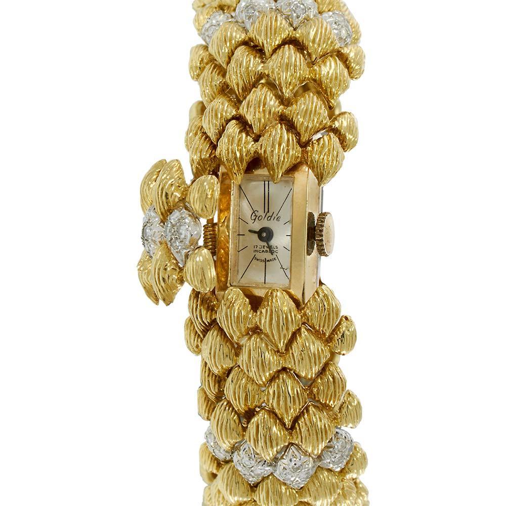 A glamorous mid-century timepiece, this 1950s Goldie Lady’s Bombe watch features an exquisite design crafted in 18KT yellow gold with a covered 14KT gold bracelet. The hinged case reveals a silver dial beneath an ornate, textured bracelet that