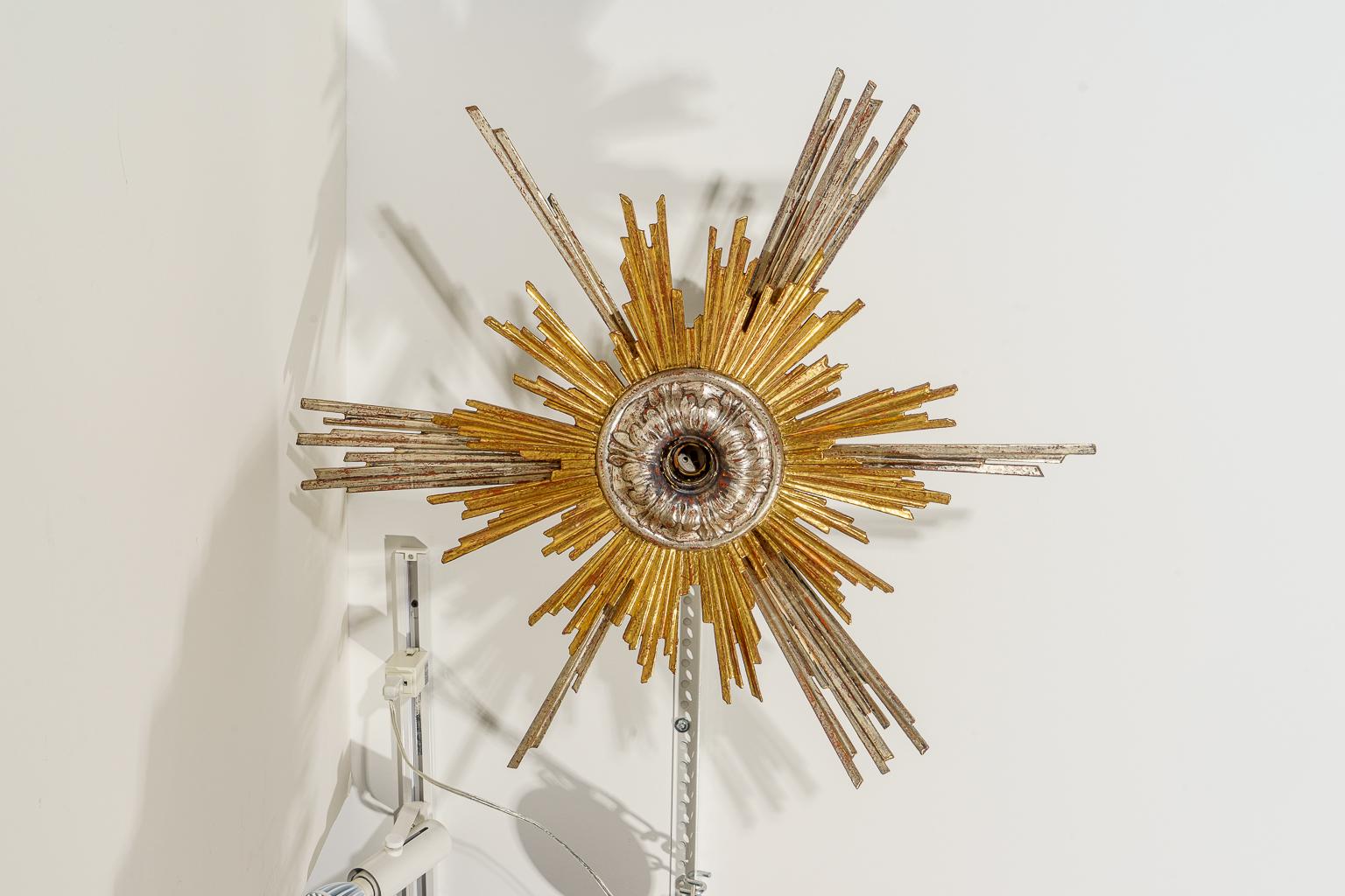 This stylish and chic starburt chandelier was acquired in Bruge, Belgium and it dates to 1900s-1920s and it is fabricated with hand carved wood sunbeams (starburst) finished in silver and gold leaf.

Note: Requires three European candelabra based